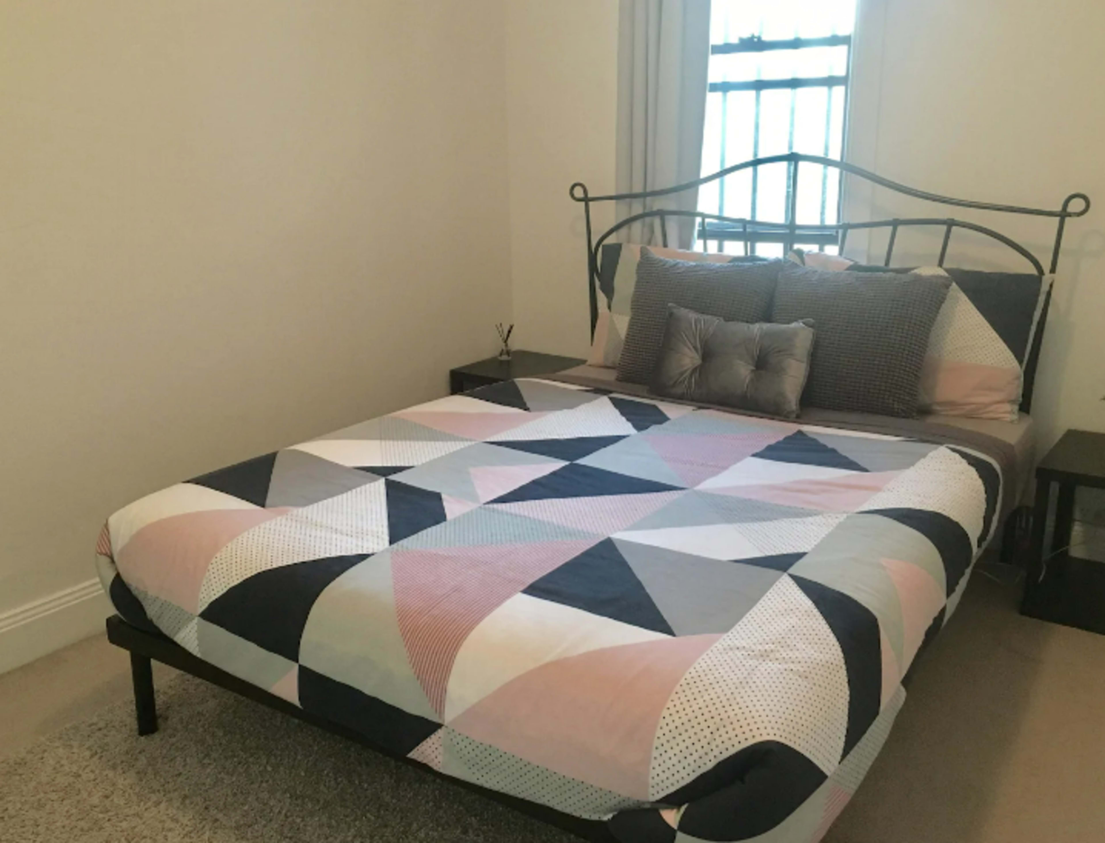A neatly made bed with a geometric patterned comforter in a simple bedroom setting.