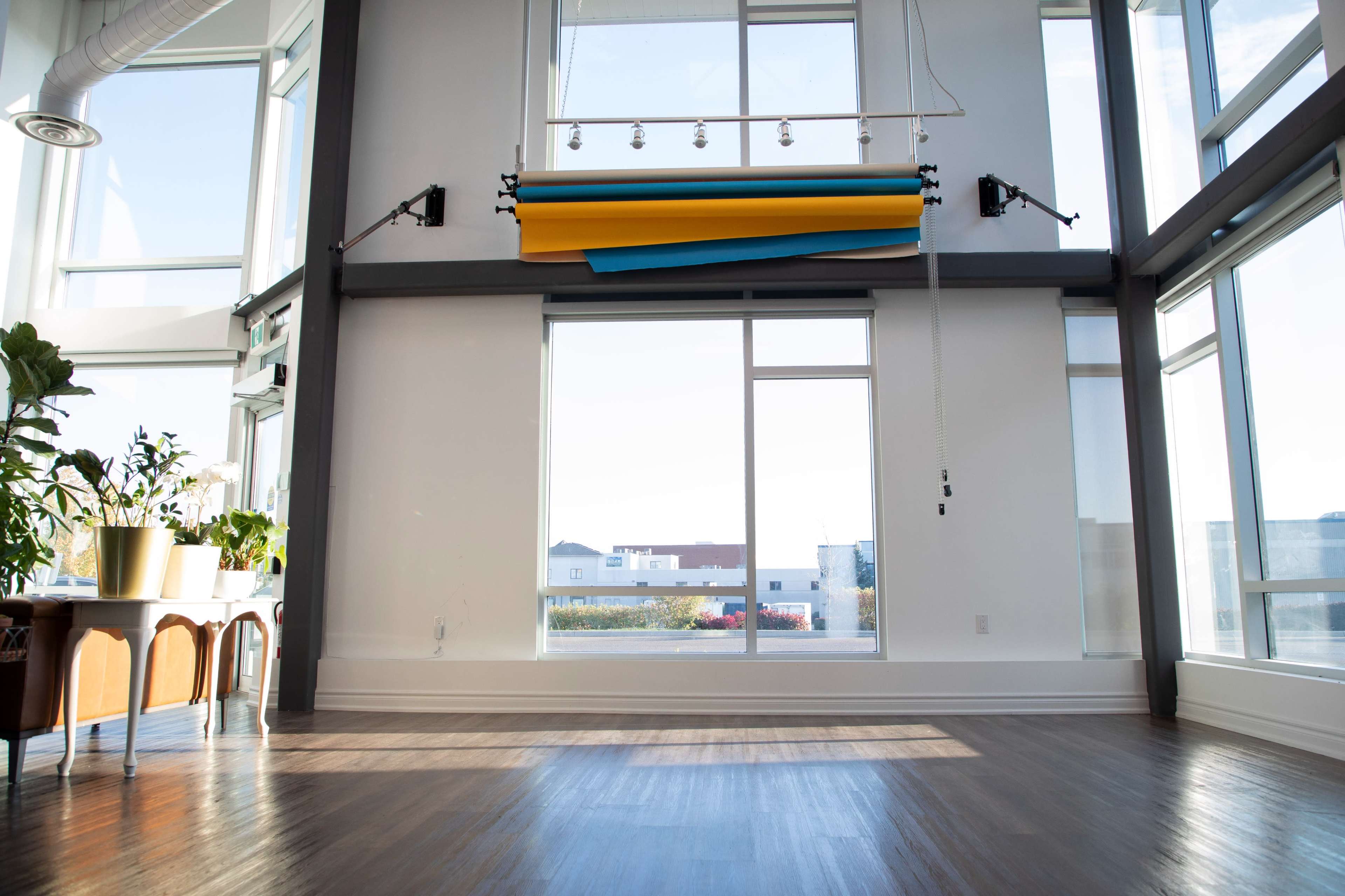 A spacious room features large windows with natural light, showcasing minimalistic furniture and a backdrop of rolled-up colored paper.