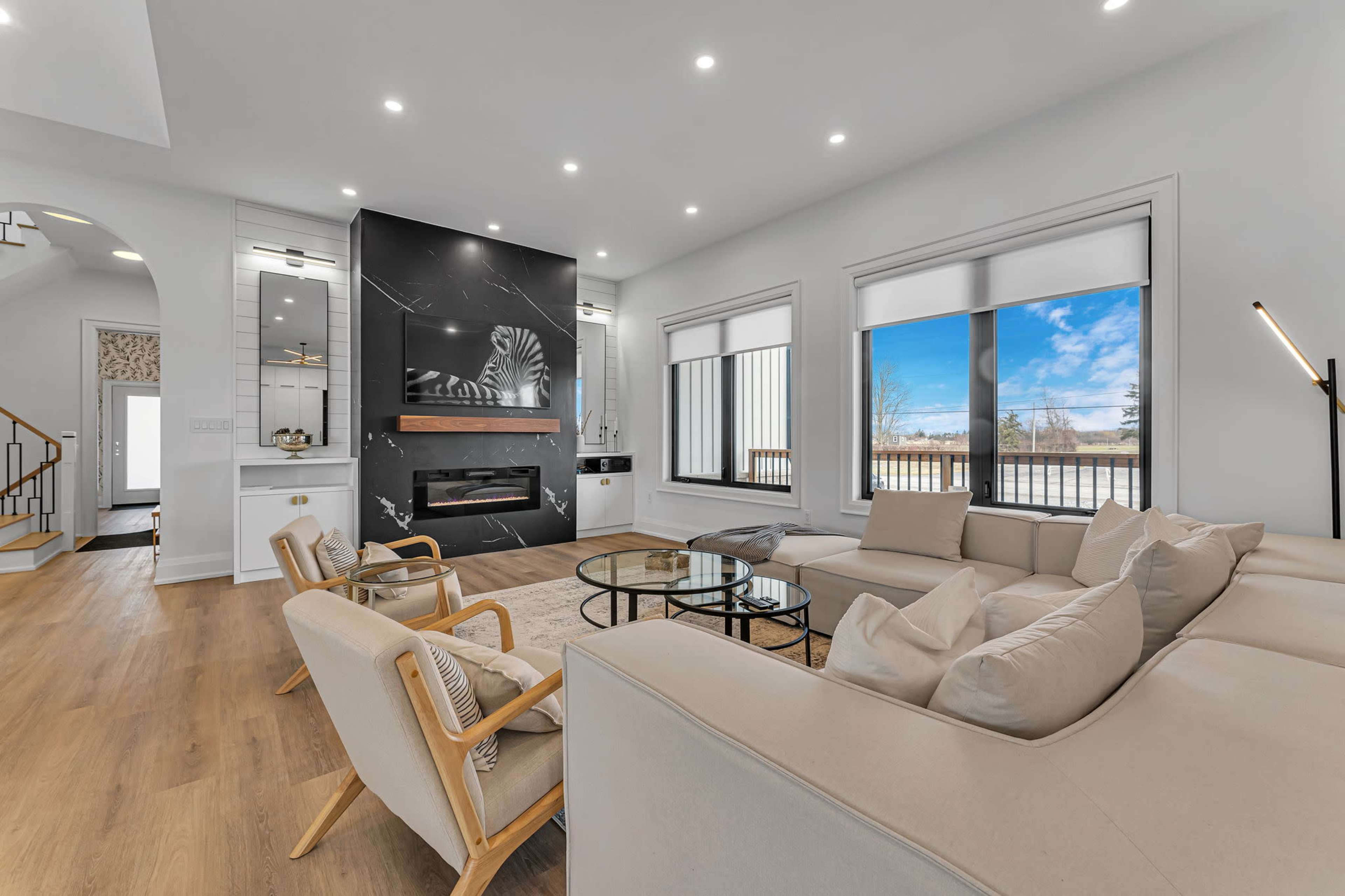 A modern living room with a large sectional sofa, a wall-mounted fireplace, and large windows that provide natural light.