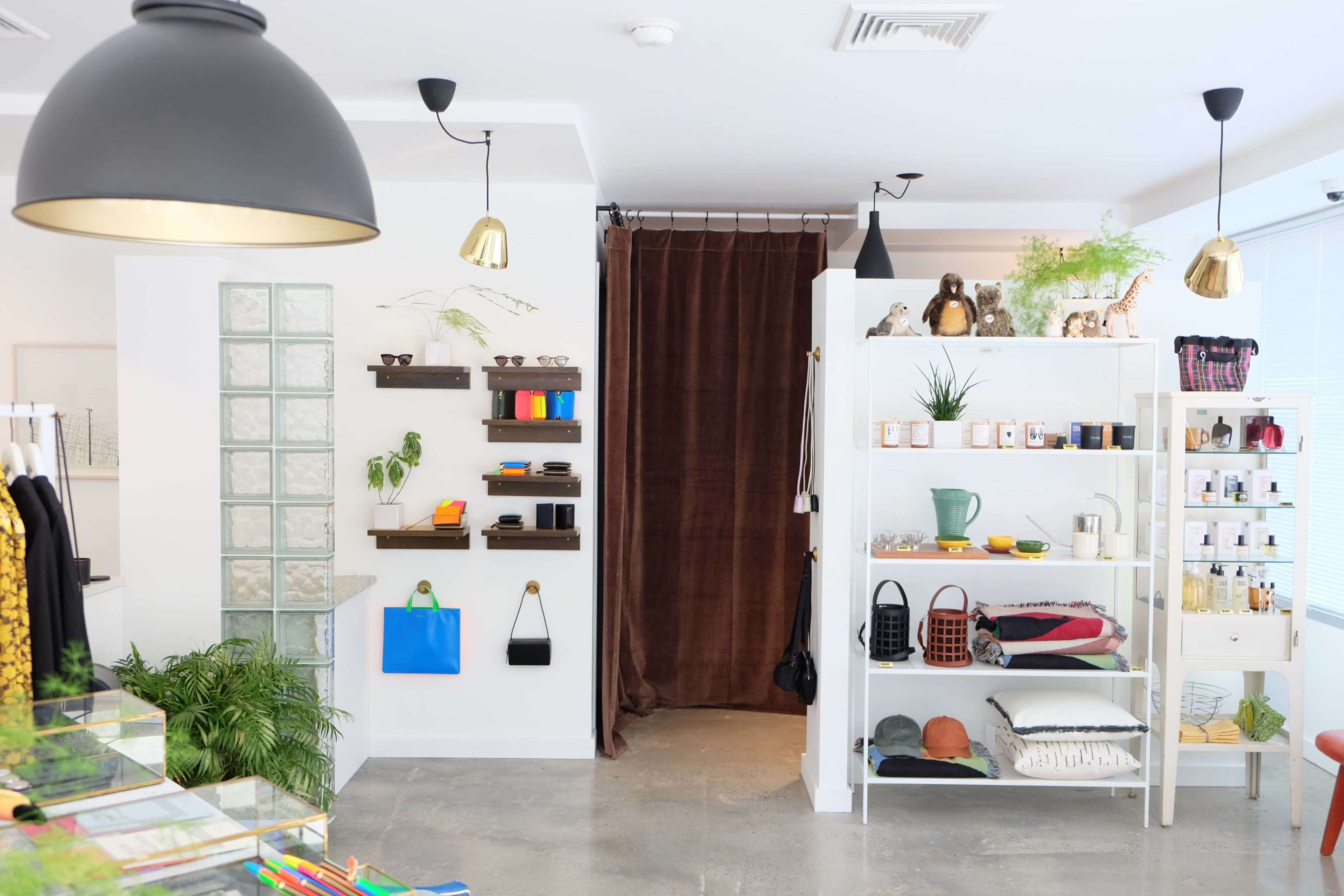 The image shows a modern retail space featuring various shelves with clothing, accessories, and decorative items, along with a curtain leading to another area.
