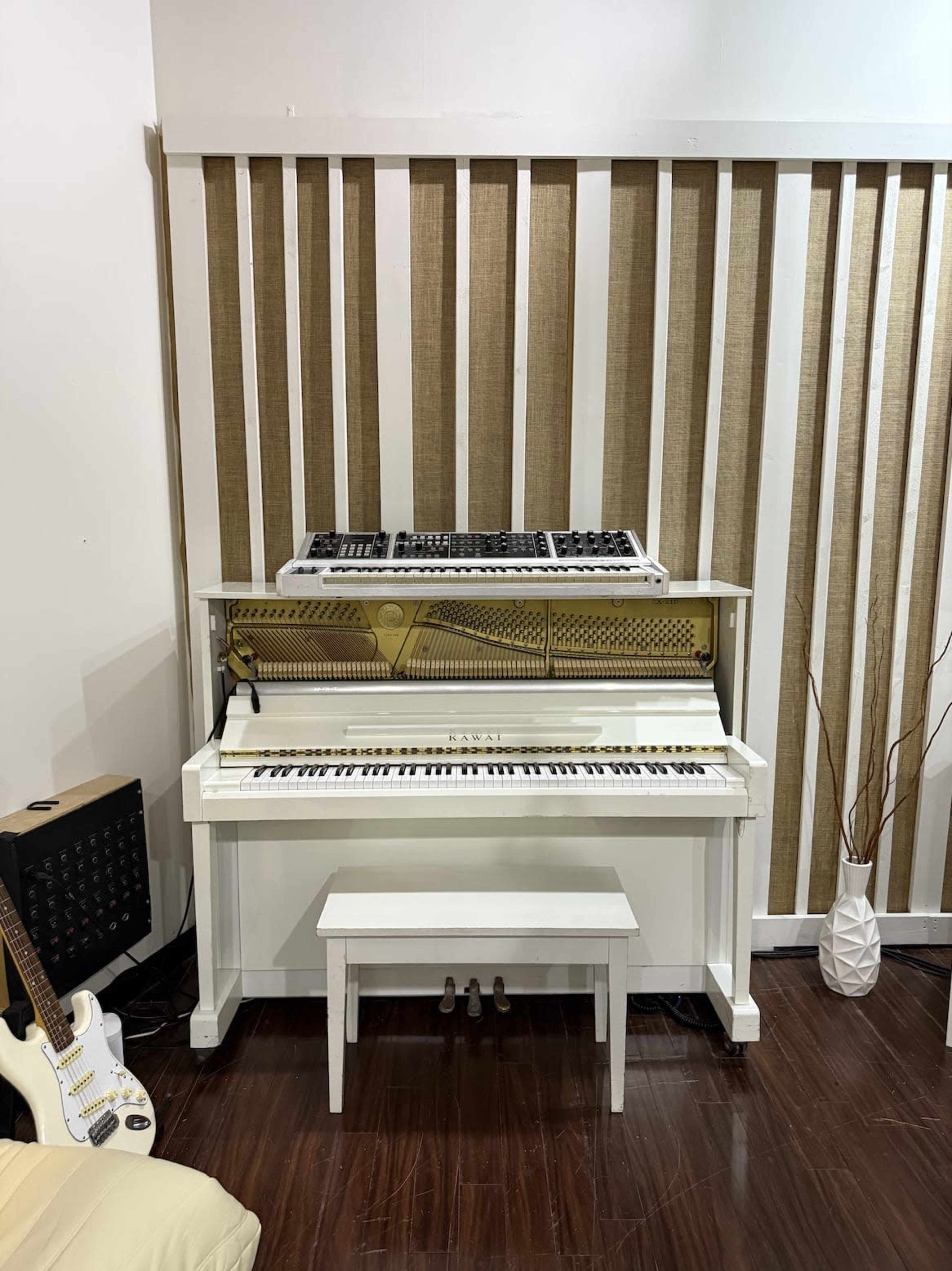 A white piano with an electronic keyboard atop it is positioned against a wall with vertical wooden slats.