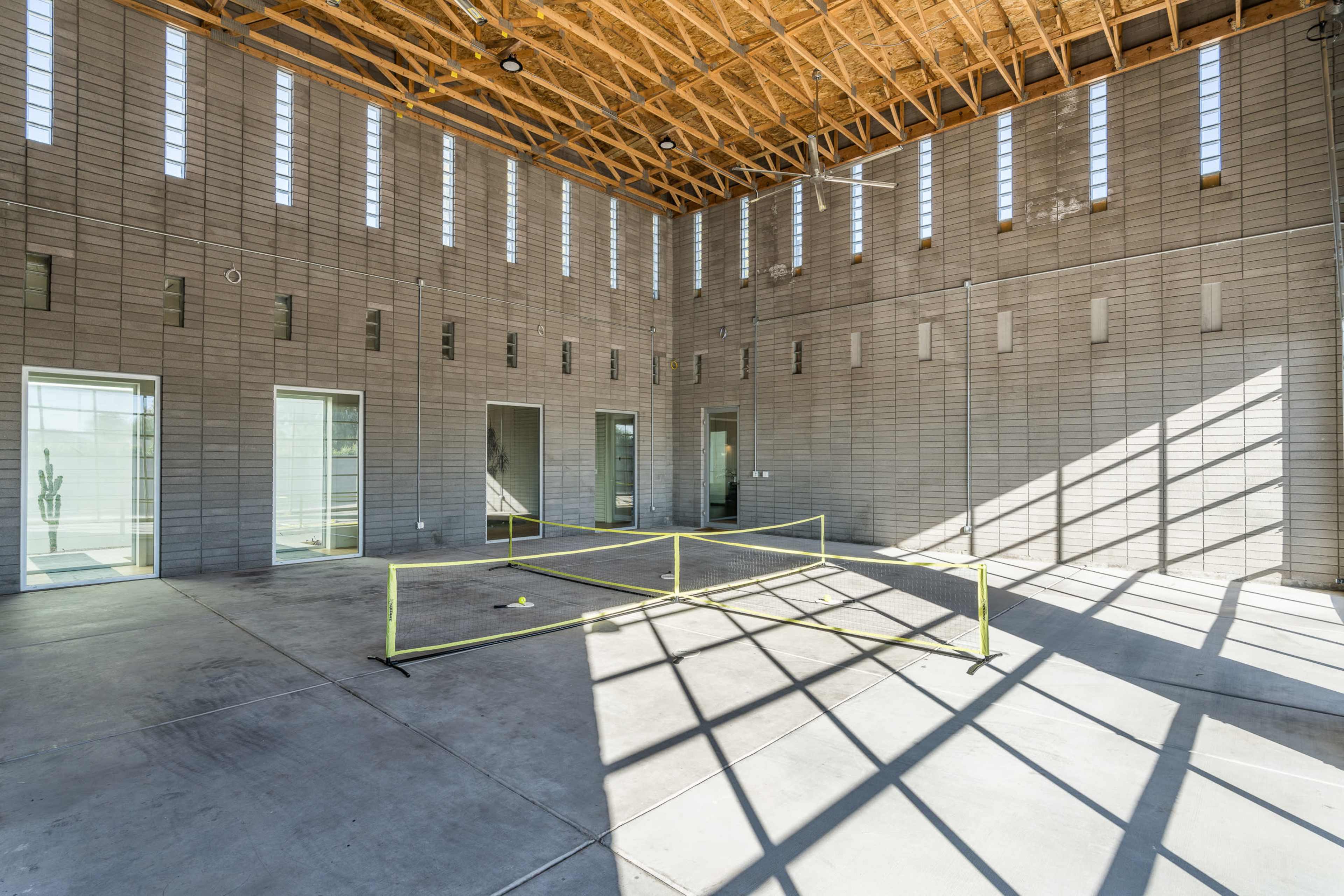 An empty interior space with concrete block walls, large windows allowing light to stream in, and a yellow safety barrier in the center of the floor.