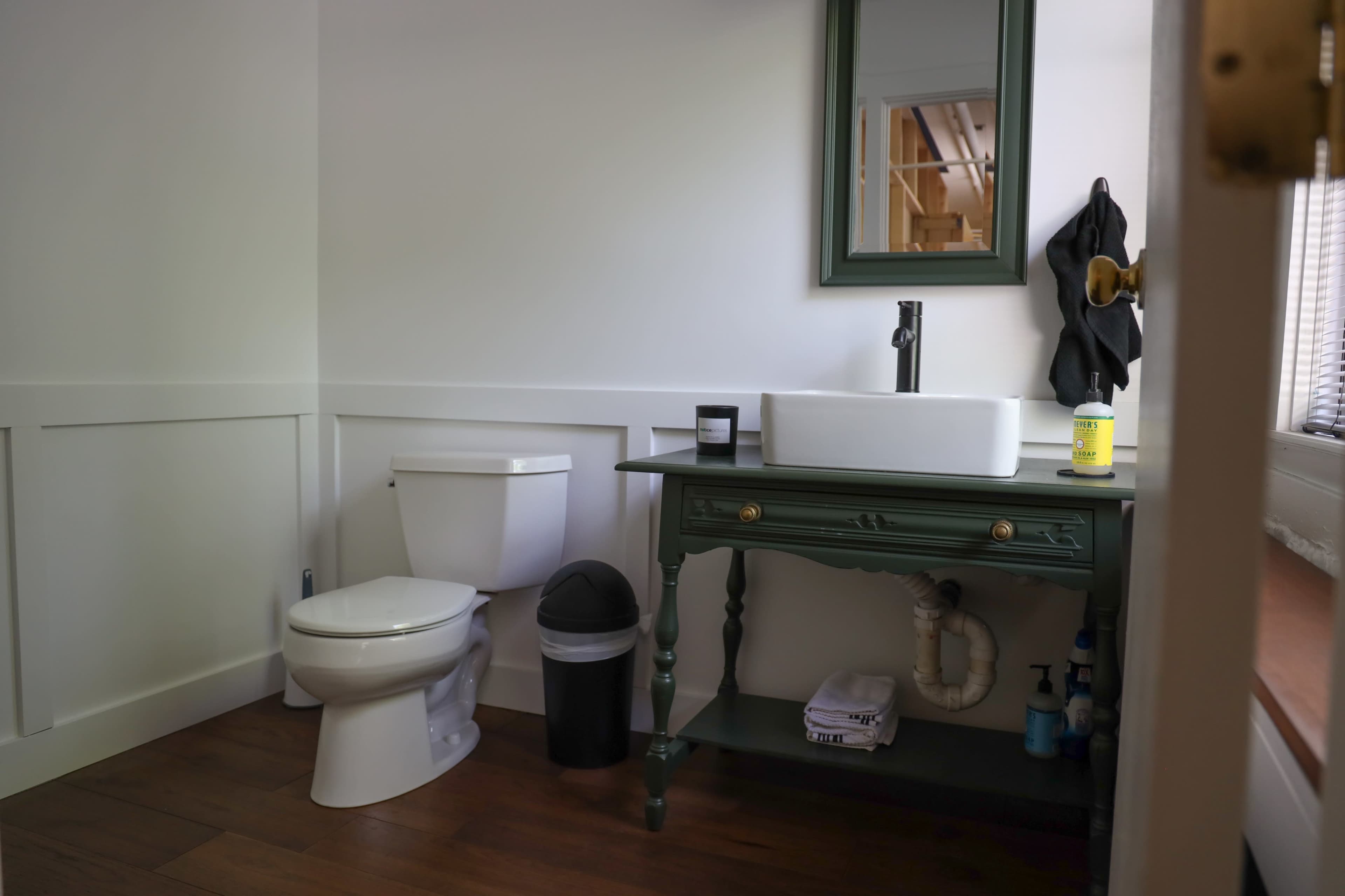 A modern bathroom features a toilet, a green vanity with a sink, and a mirror on the wall.