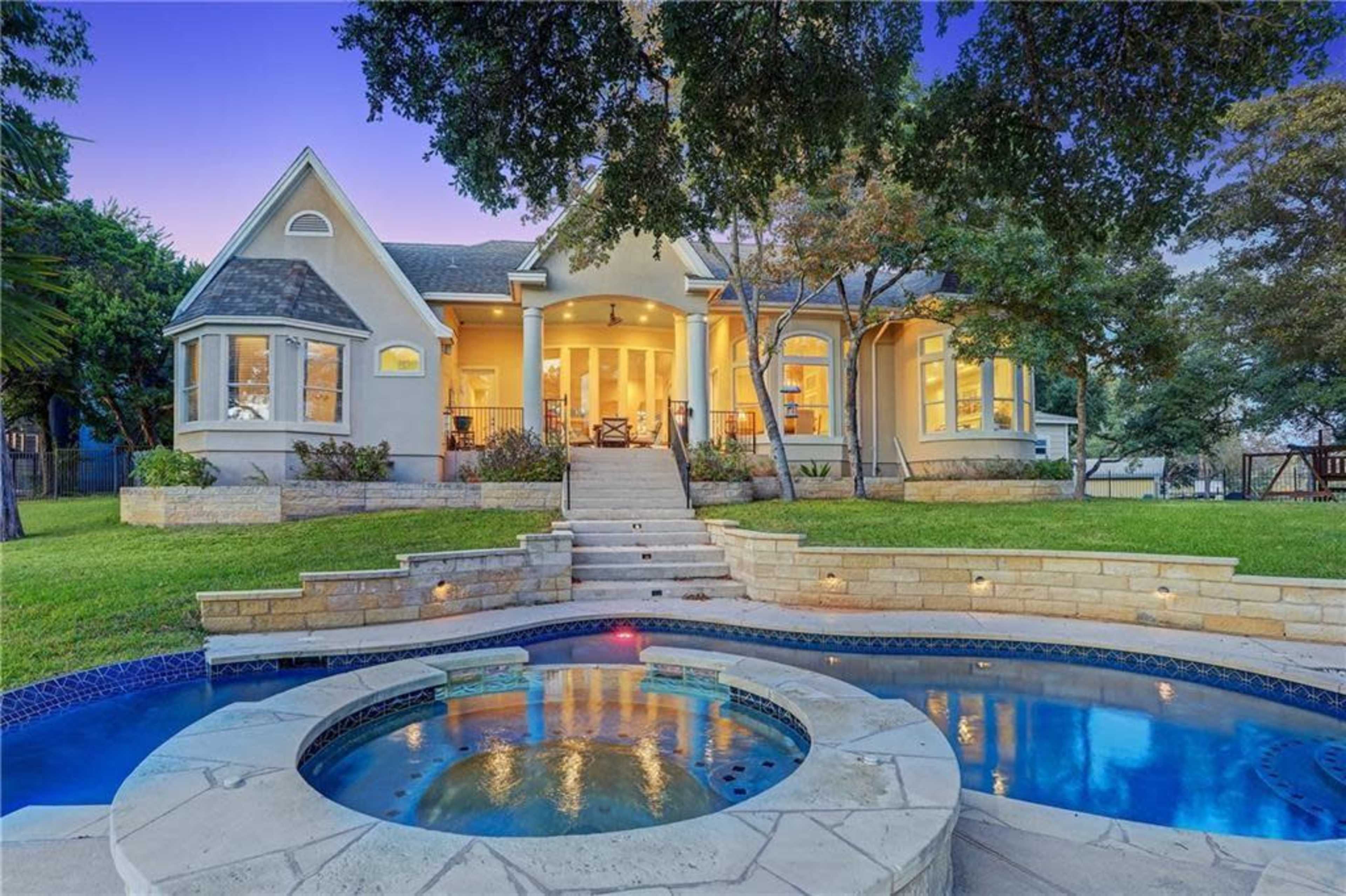 A two-story house with large windows and a stone pathway leads to a landscaped yard featuring a pool and a hot tub.