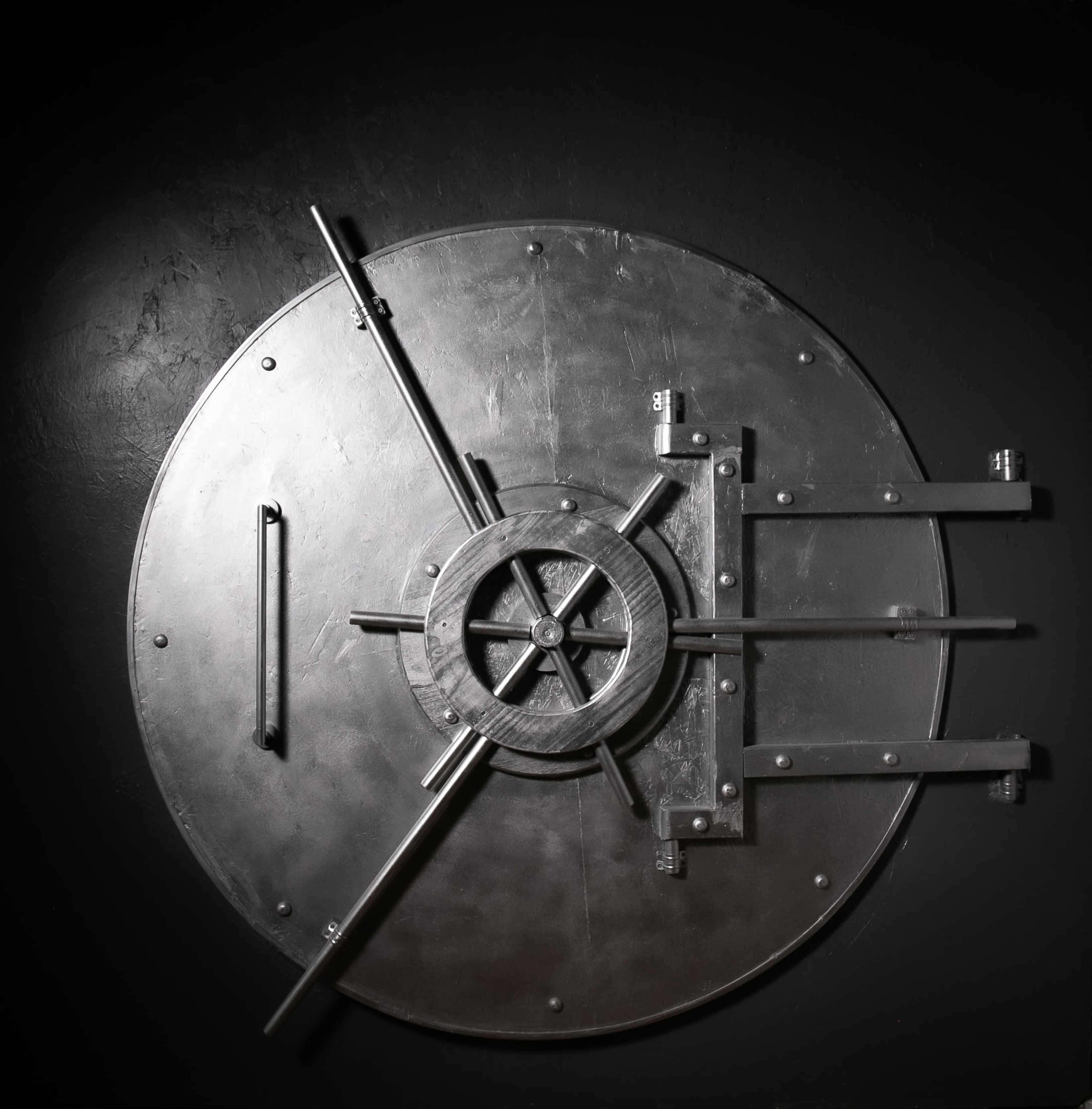 The image shows a large metallic safe door mounted against a dark background.