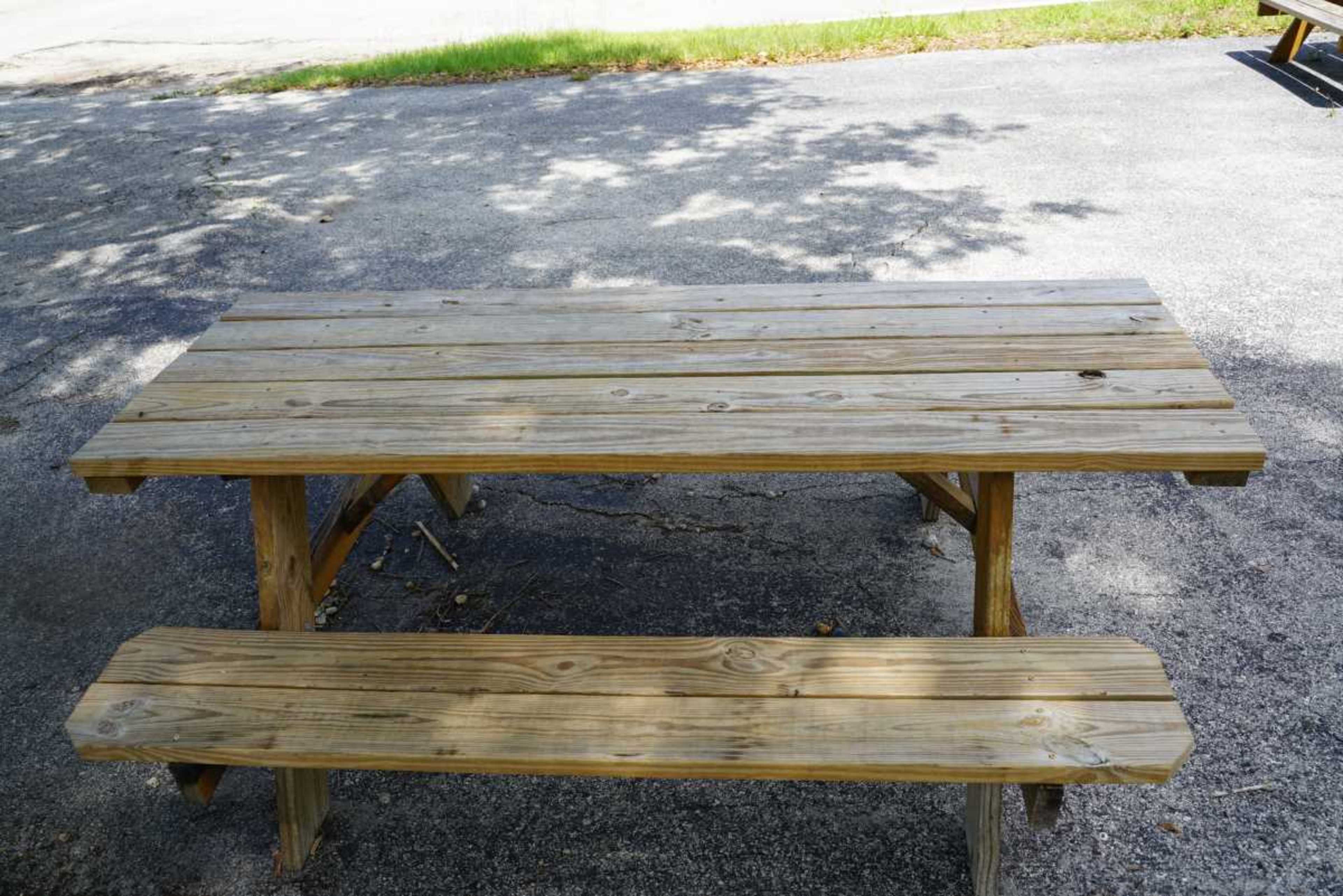 A wooden picnic table with a bench sits on a paved surface surrounded by grass.
