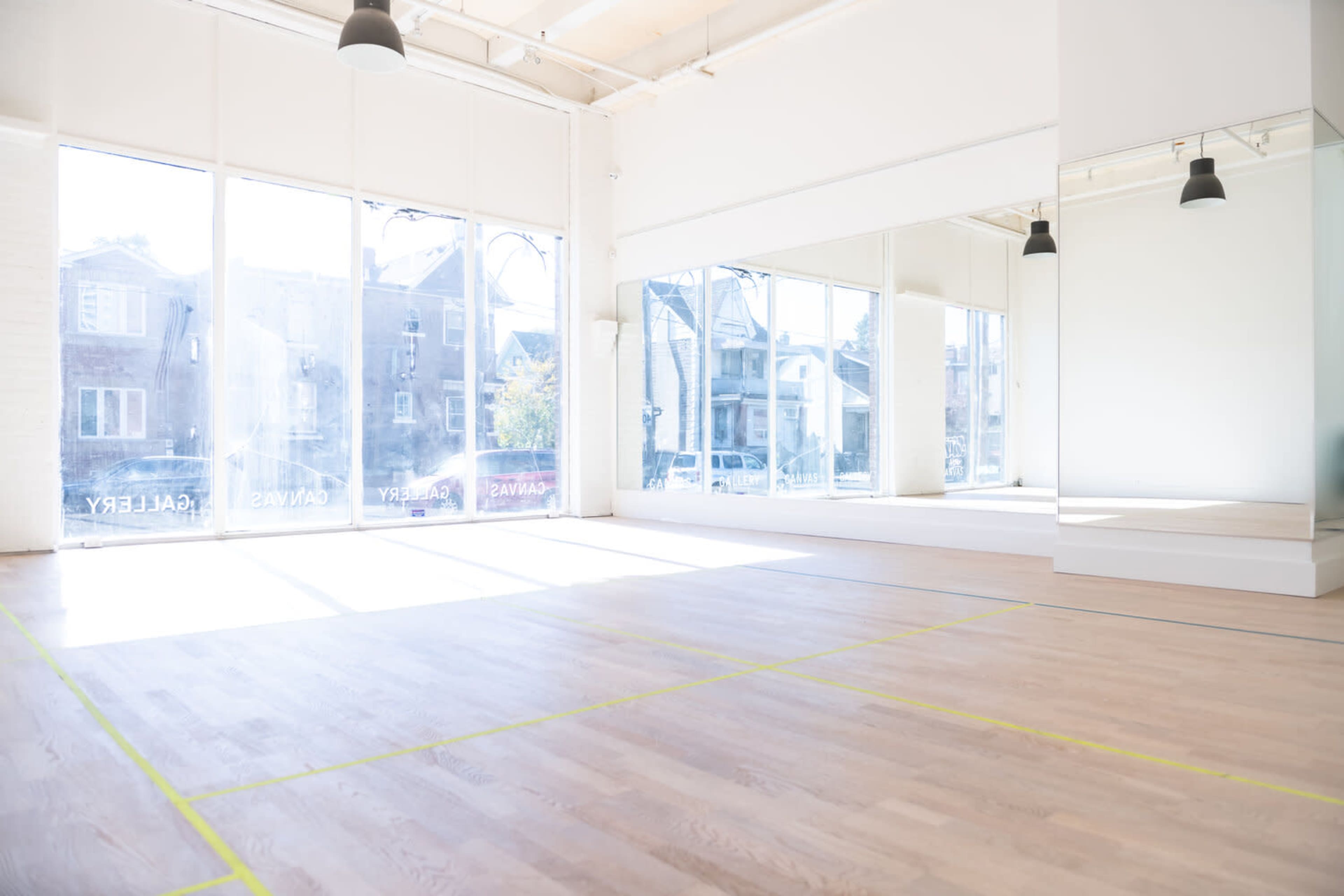 A spacious, well-lit empty studio with large windows and a mirrored wall.