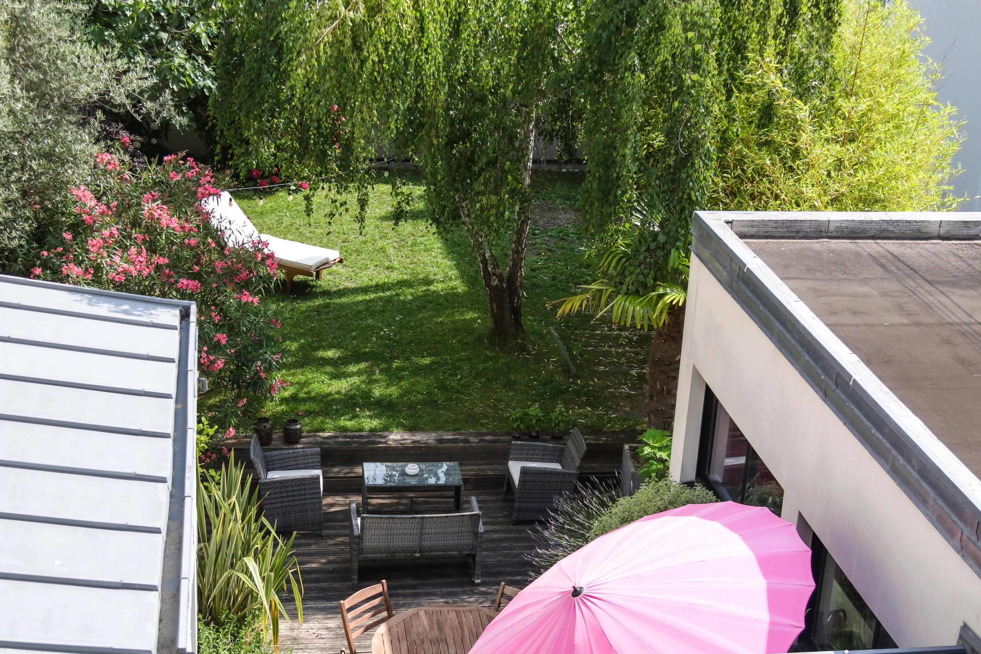 A landscaped backyard featuring green grass, patio furniture, and a large pink umbrella.