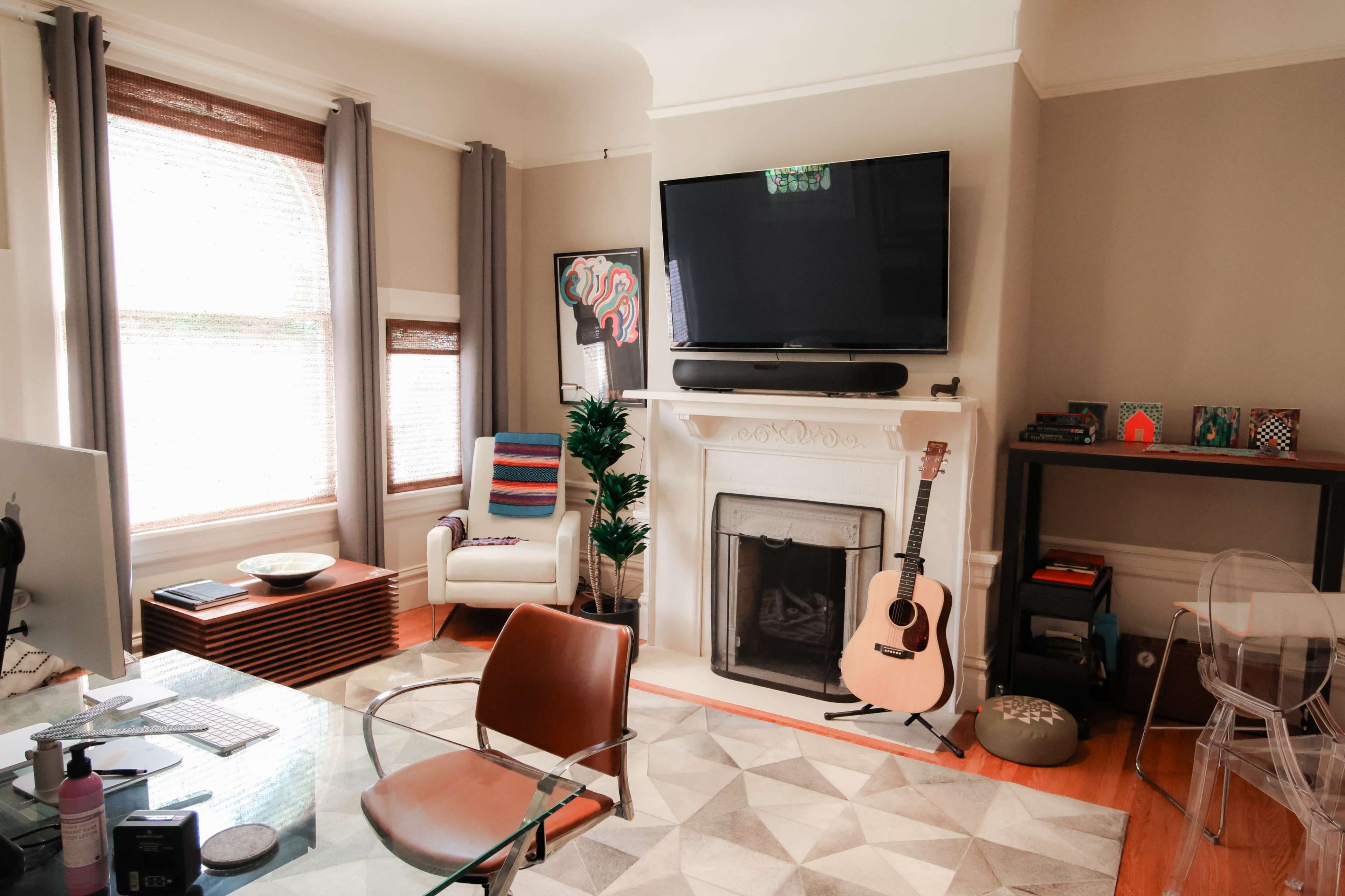 A modern living room featuring a fireplace, a wall-mounted television, a guitar, and a glass table with chairs.