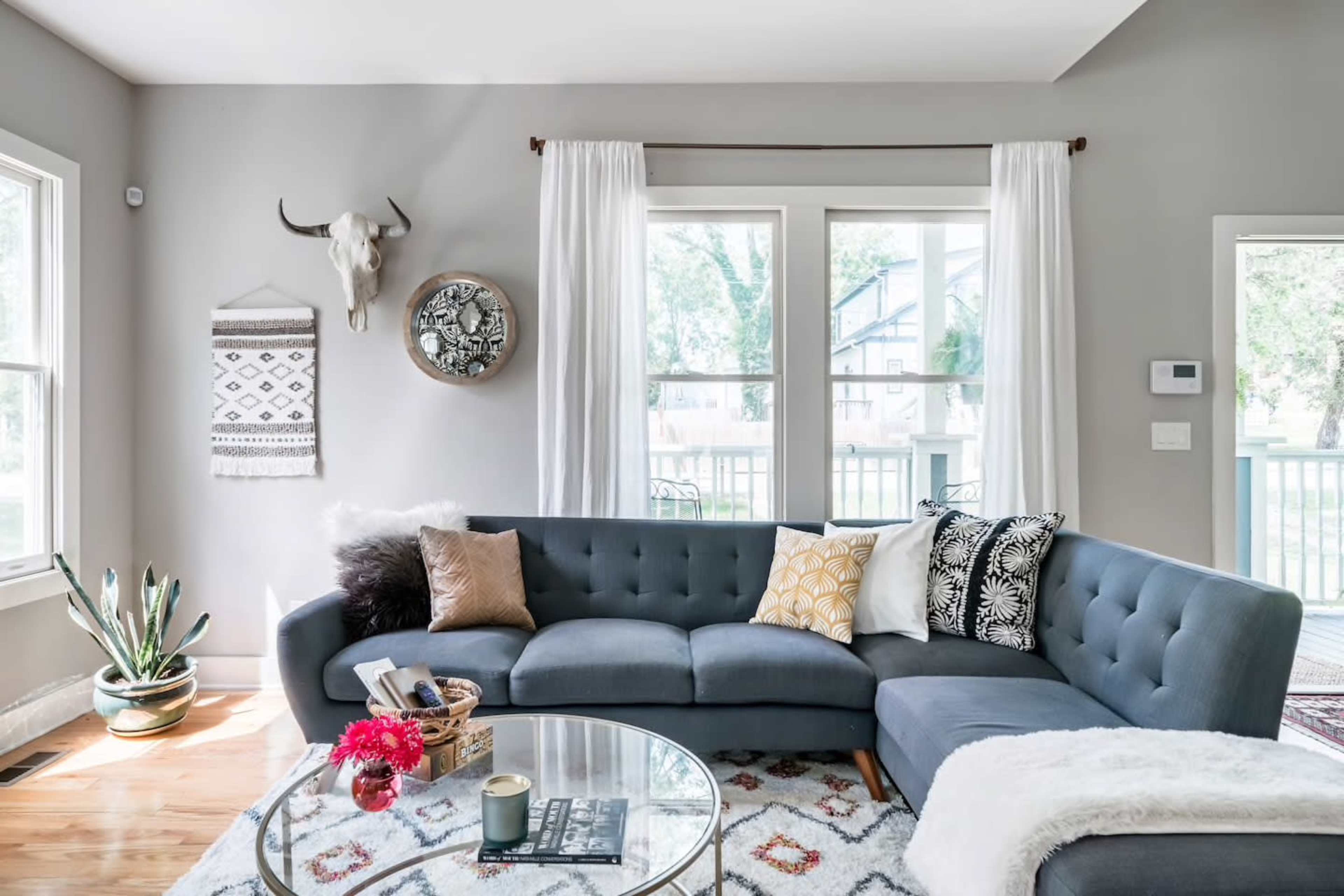 A cozy living room featuring a sectional sofa, a round coffee table, decorative pillows, and large windows that provide natural light.