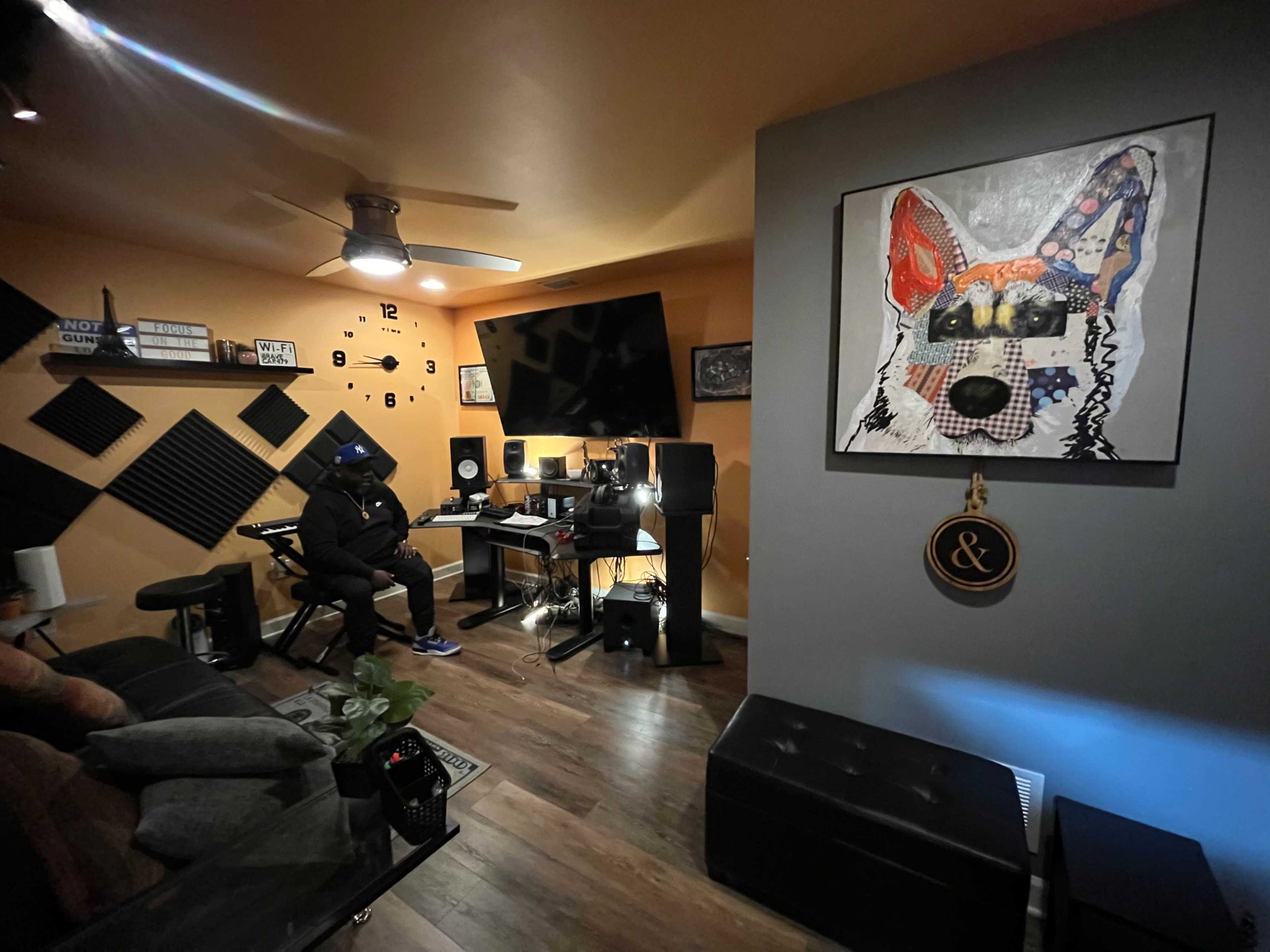 A person sits at a computer workstation in a music production studio, featuring soundproof panels and modern decor.