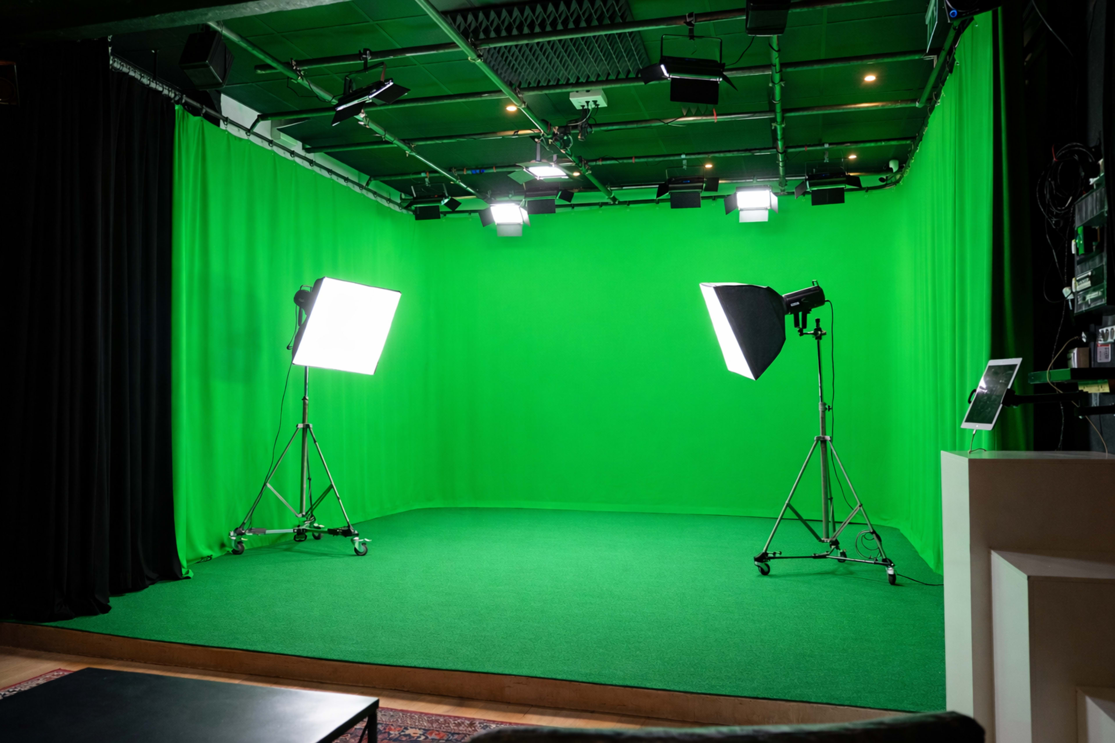 The image shows a green screen studio with two lighting setups on stands and black curtains surrounding the area.