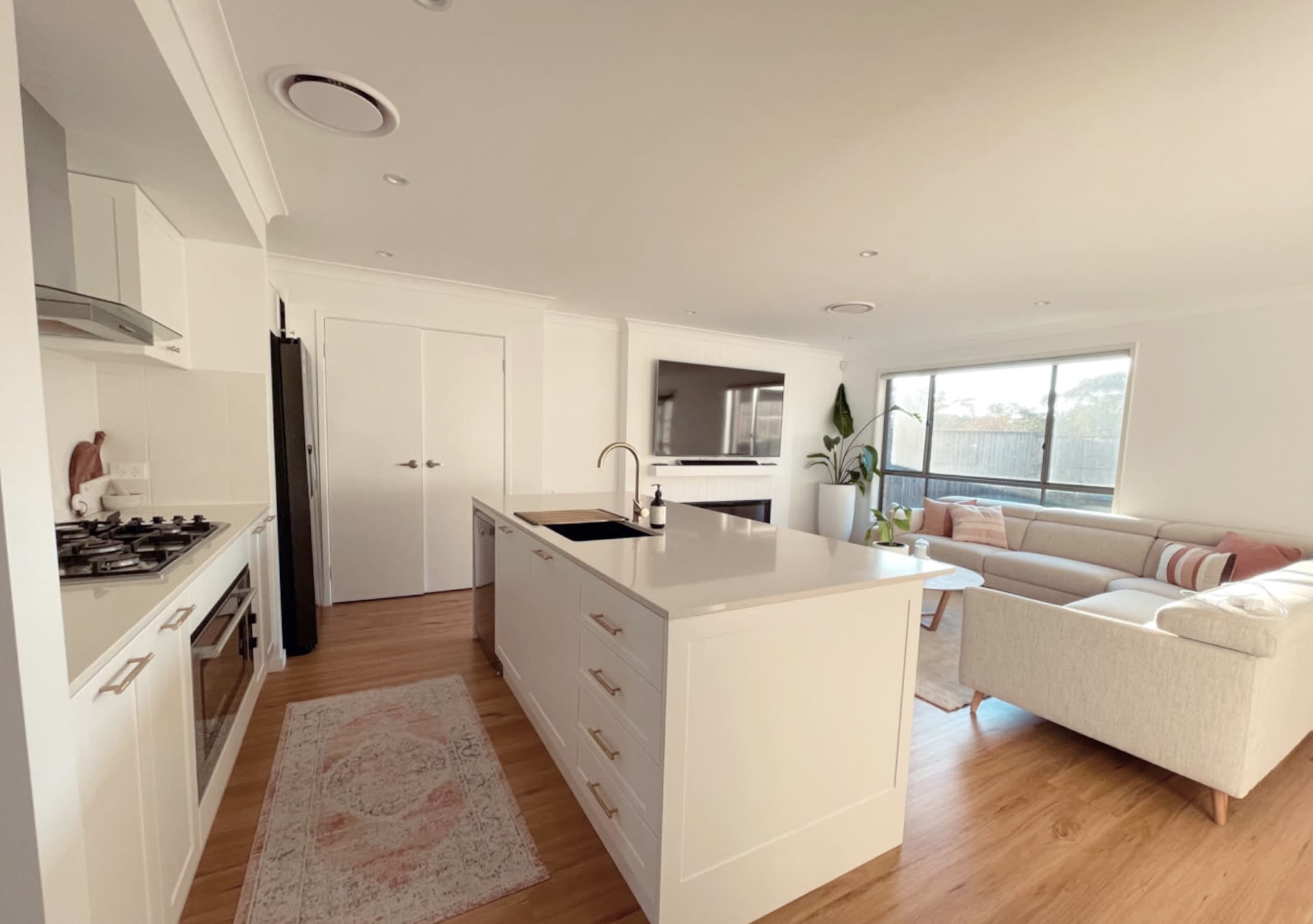 The image shows a modern kitchen and living area with a white kitchen island, a gas stove, and a comfortable sofa next to large windows.