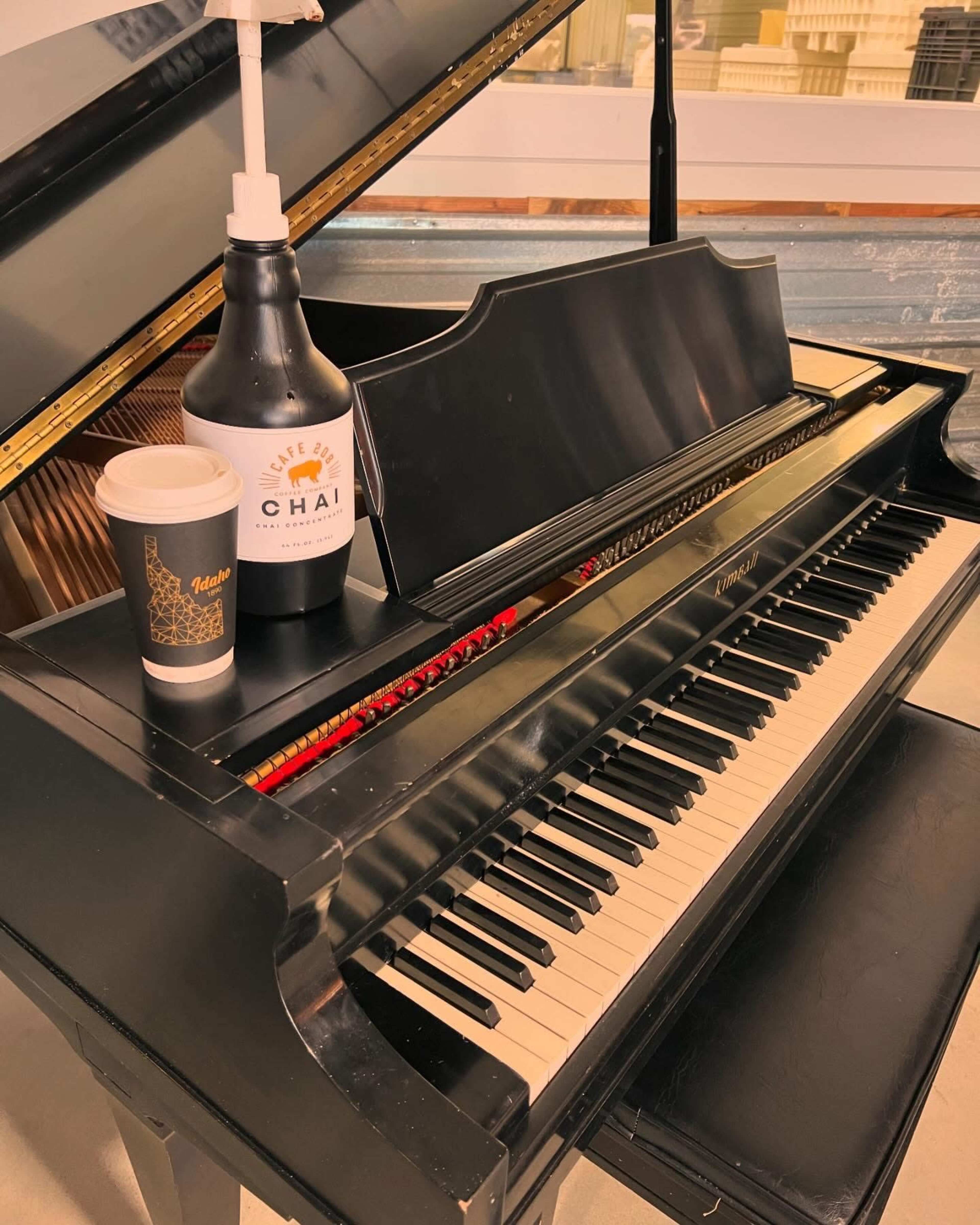 A black piano with visible keys hosts a coffee cup and a bottle labeled "Chai" on top of it.