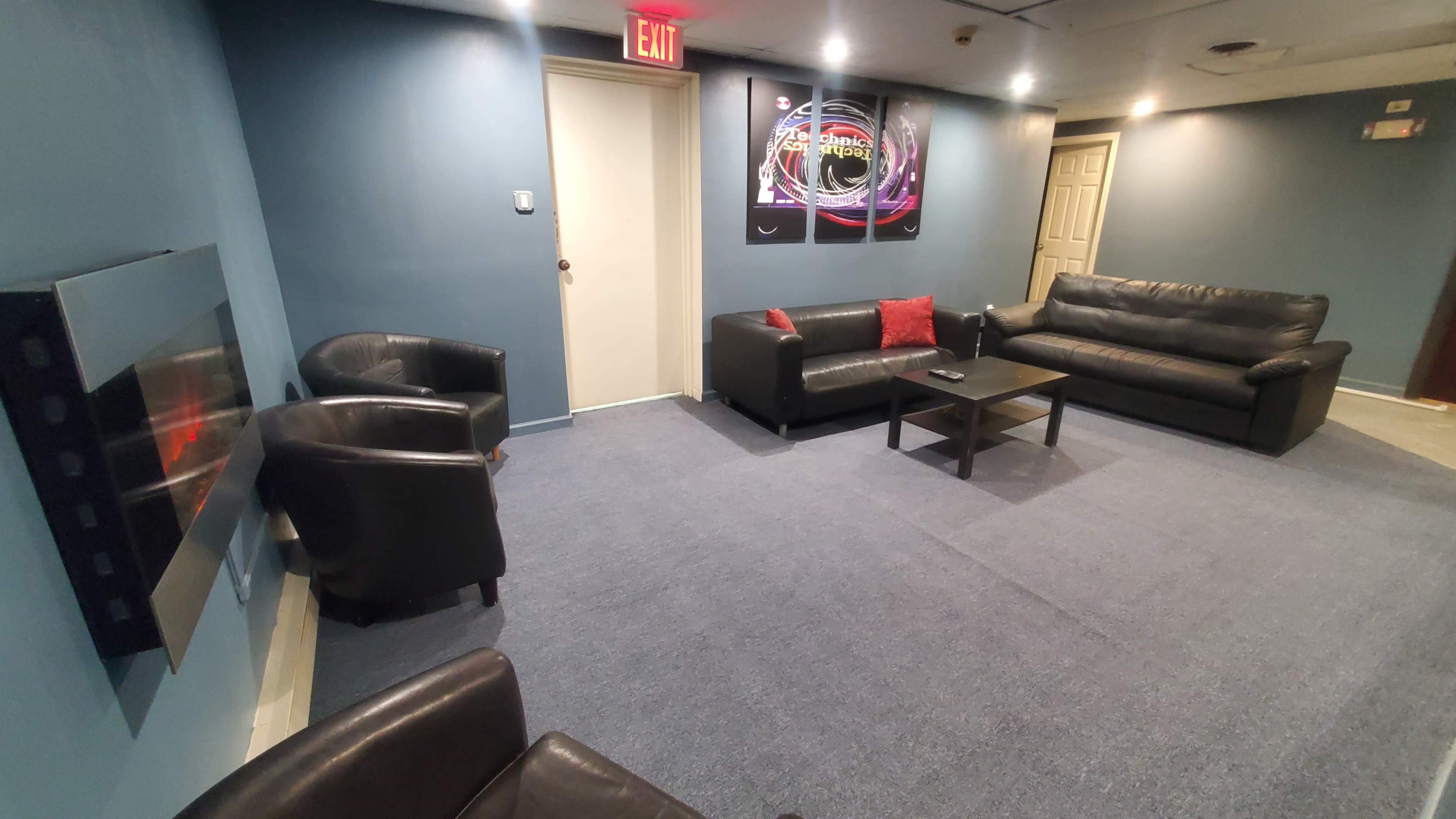 A waiting room with black leather sofas and chairs arranged around a central coffee table, featuring blue walls and a wall-mounted decor piece.