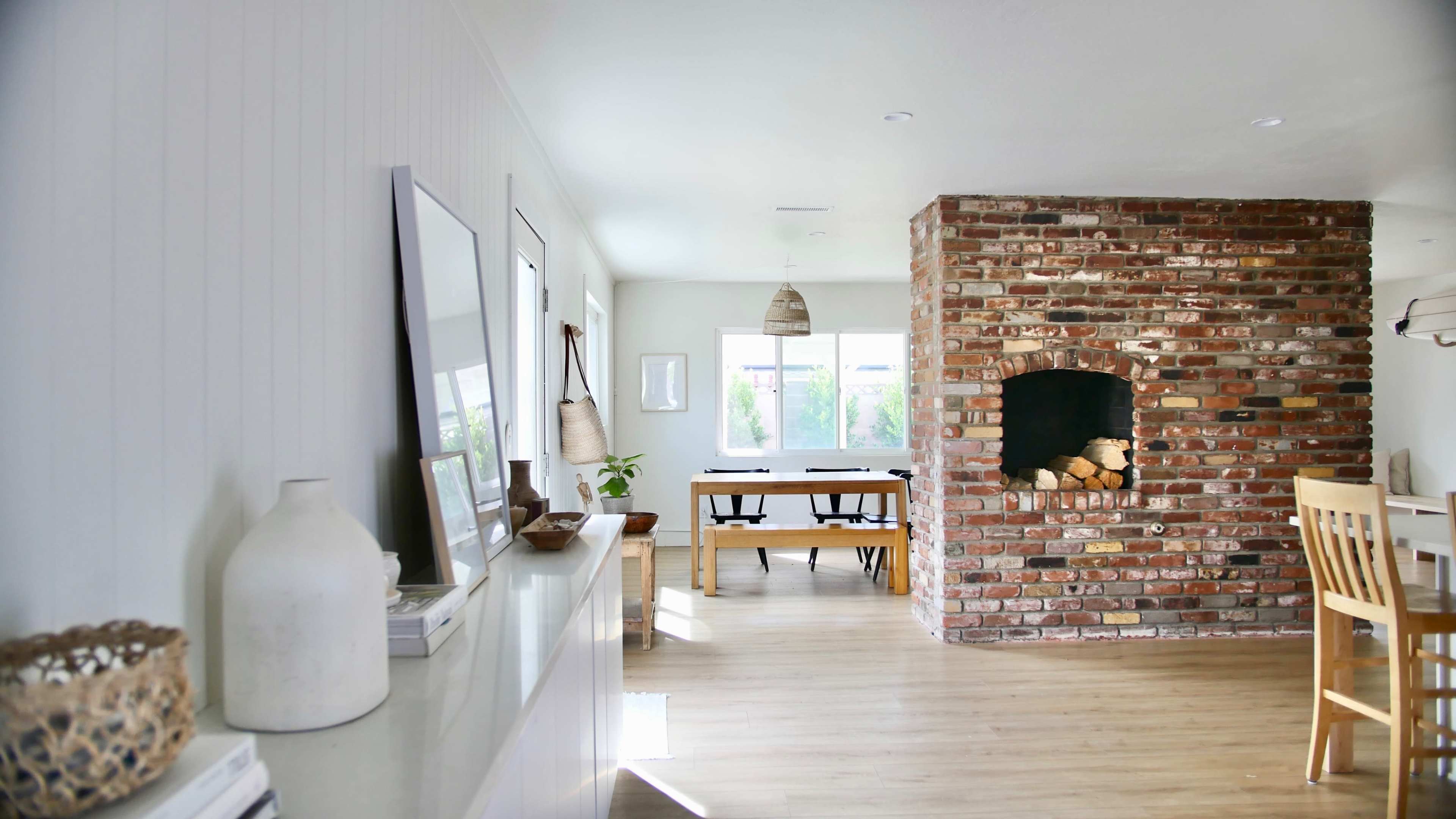 A bright, modern living space features a brick fireplace, wooden dining table, and light-colored walls.
