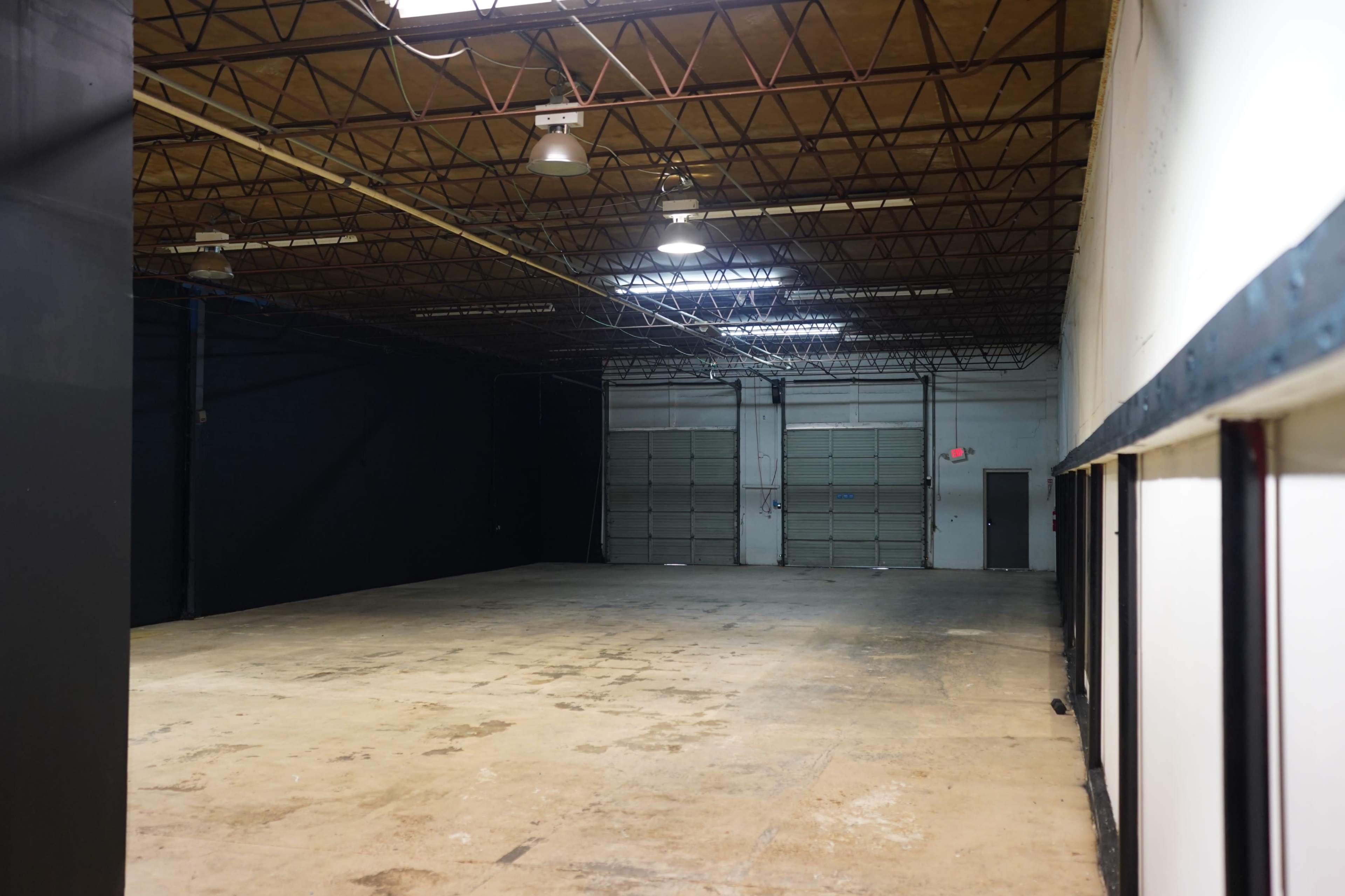 The image shows a large, empty warehouse space with a concrete floor and overhead lighting.