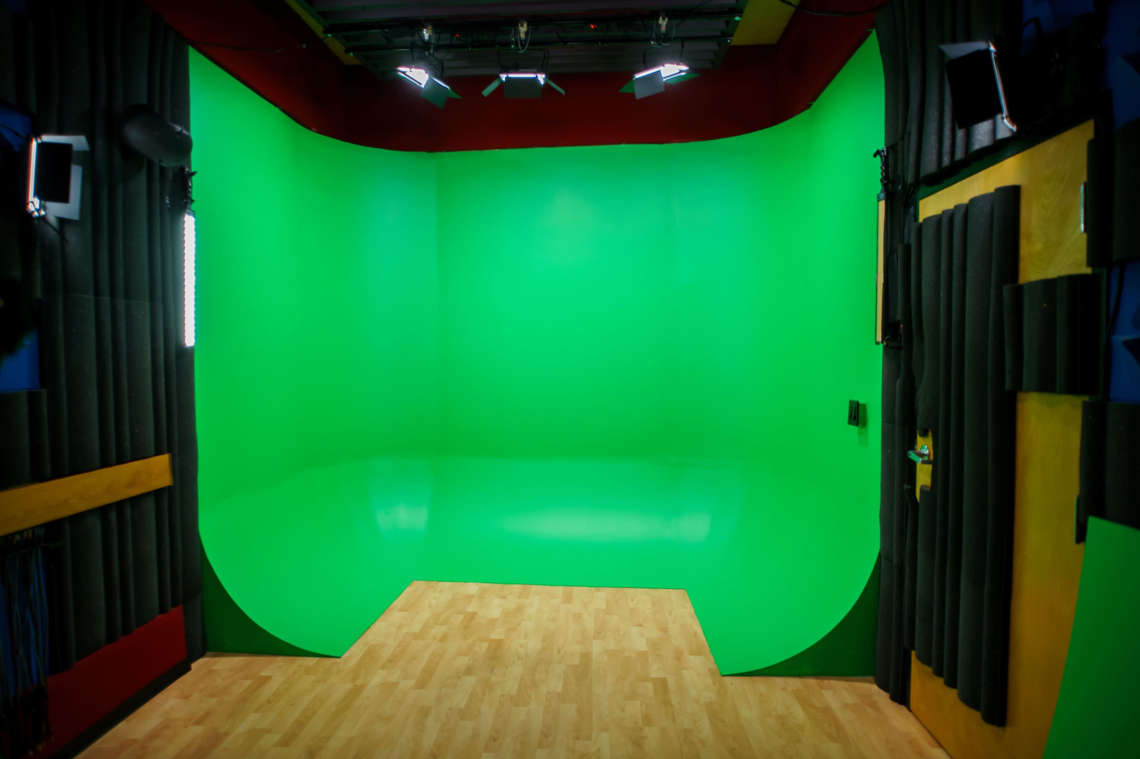 A green screen studio with a curved green backdrop and wooden flooring.