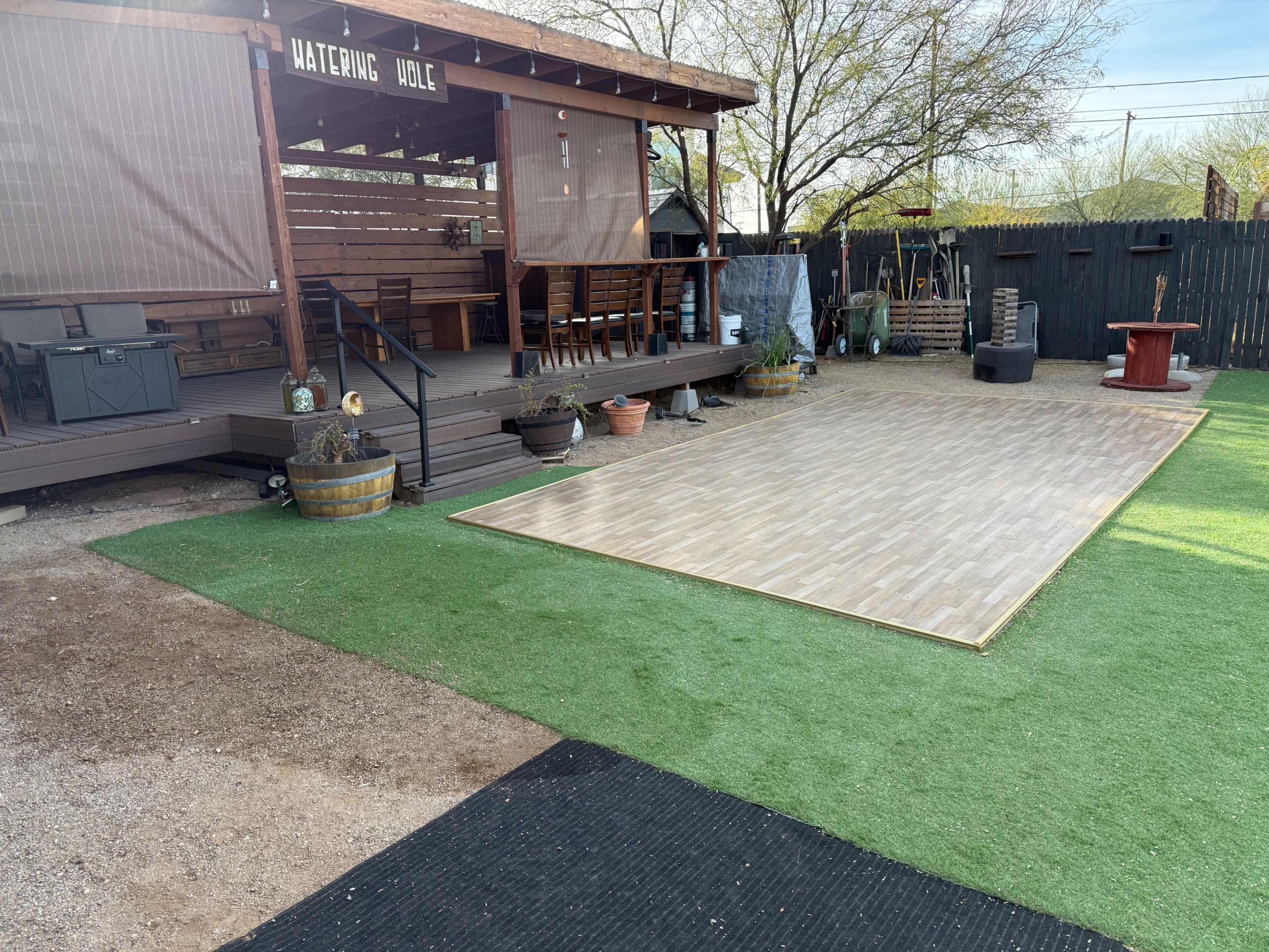The image shows a backyard patio area with a wooden deck, an artificial grass section, and a wooden floor framework being constructed.
