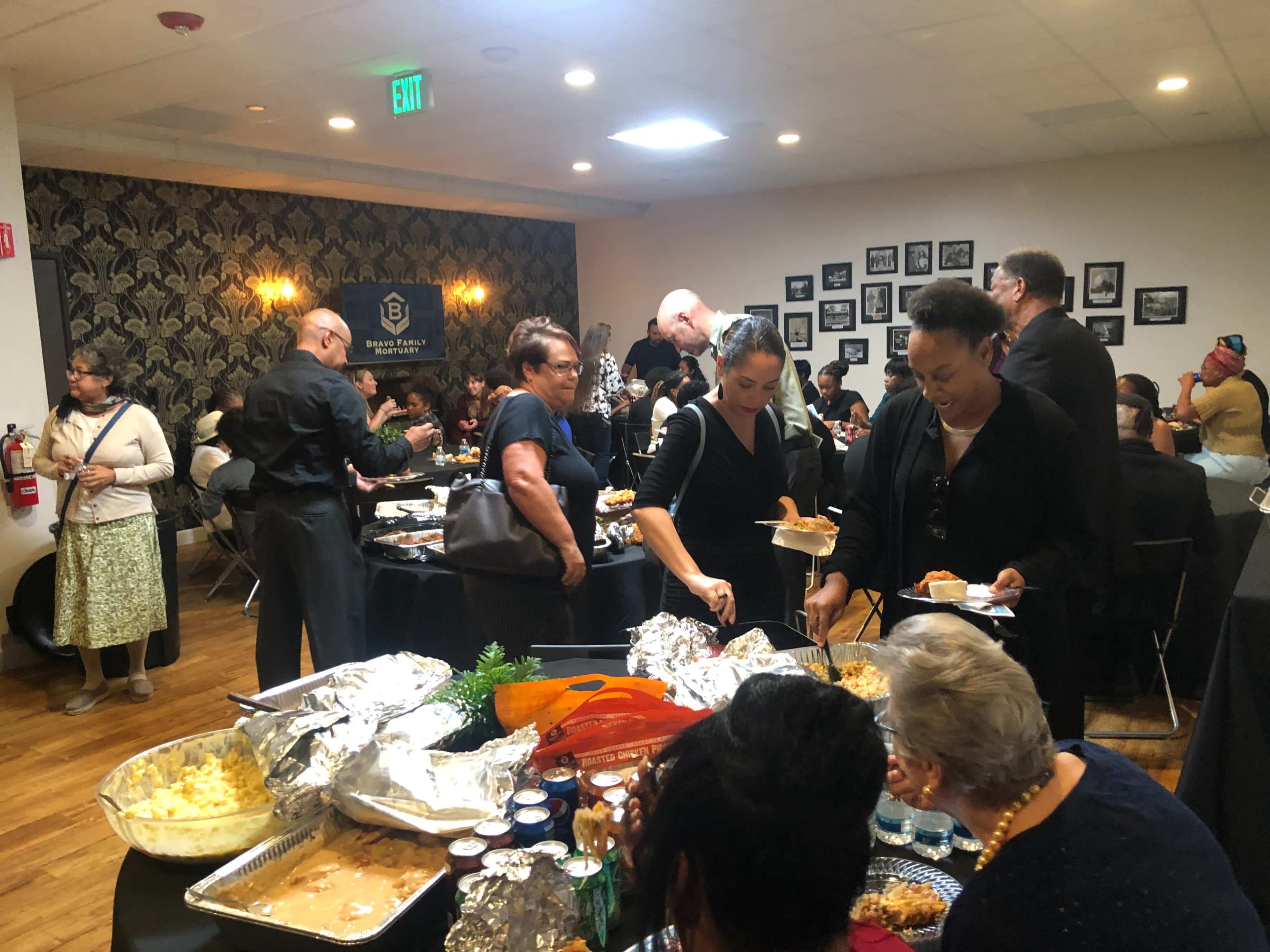A large group of people is gathering around a buffet table filled with food at an indoor event.