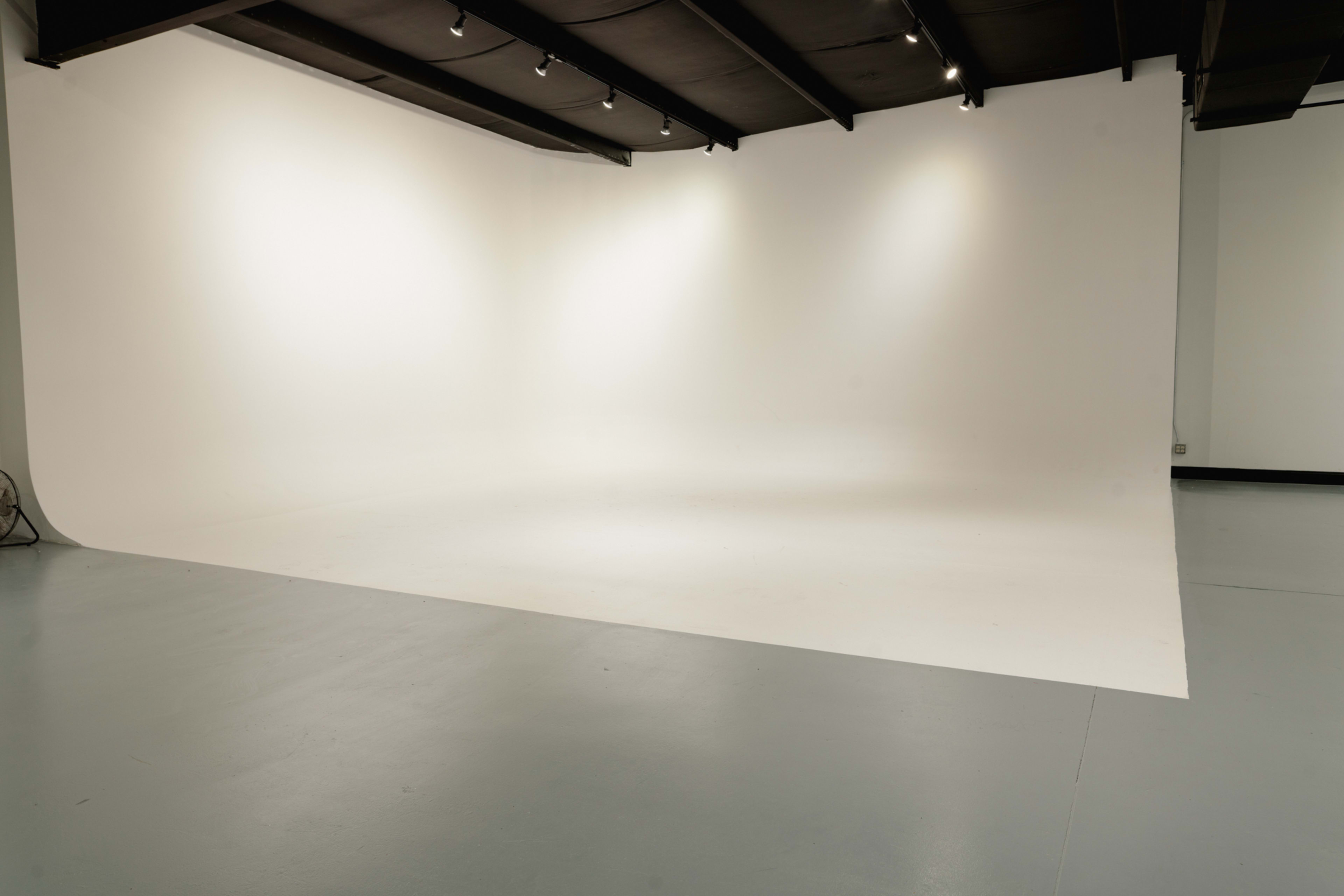 The image shows a spacious photography studio with a seamless white background and smooth, light-colored flooring.
