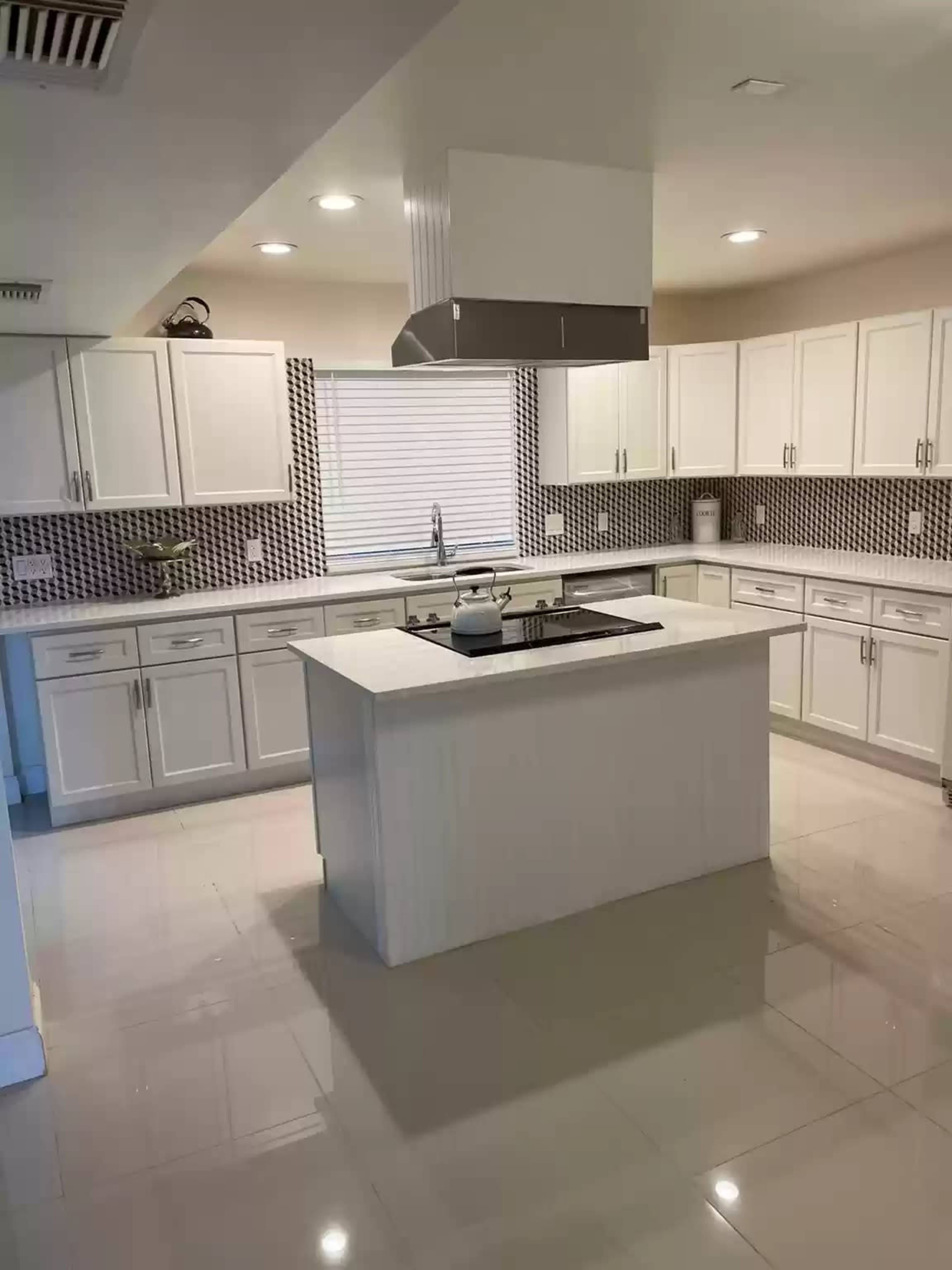 A modern kitchen with white cabinets, a central island, and a patterned backsplash.