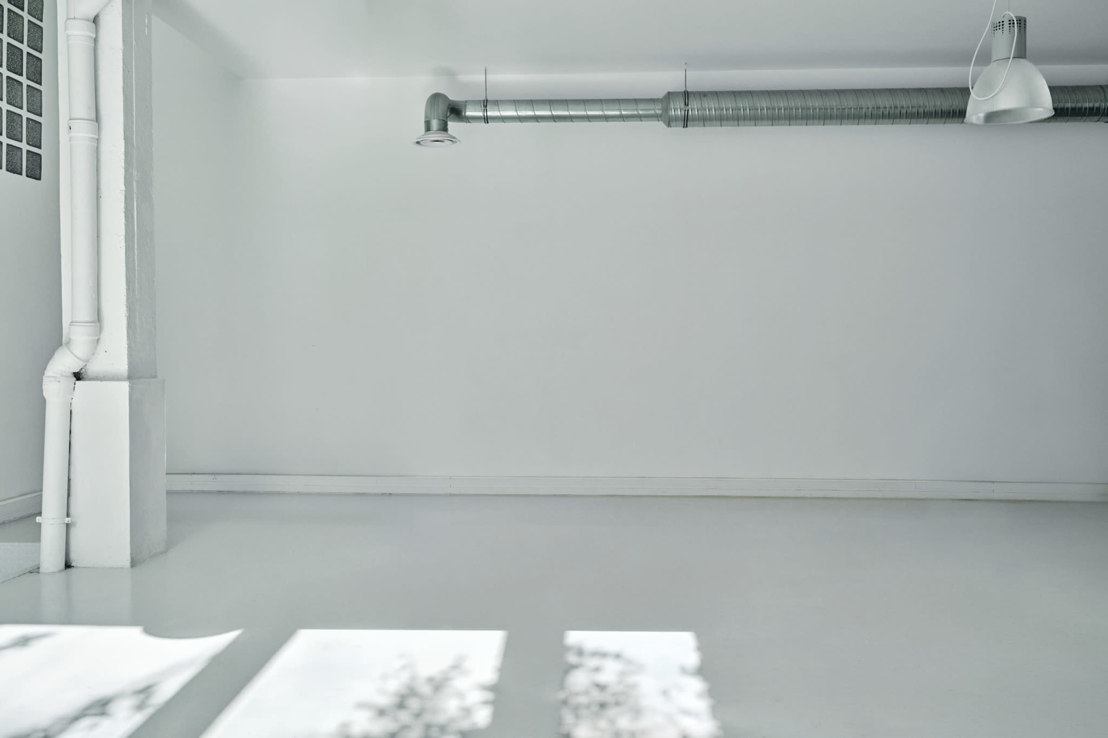 The image shows a bright, minimalistic room with white walls, a polished floor, and exposed ductwork.