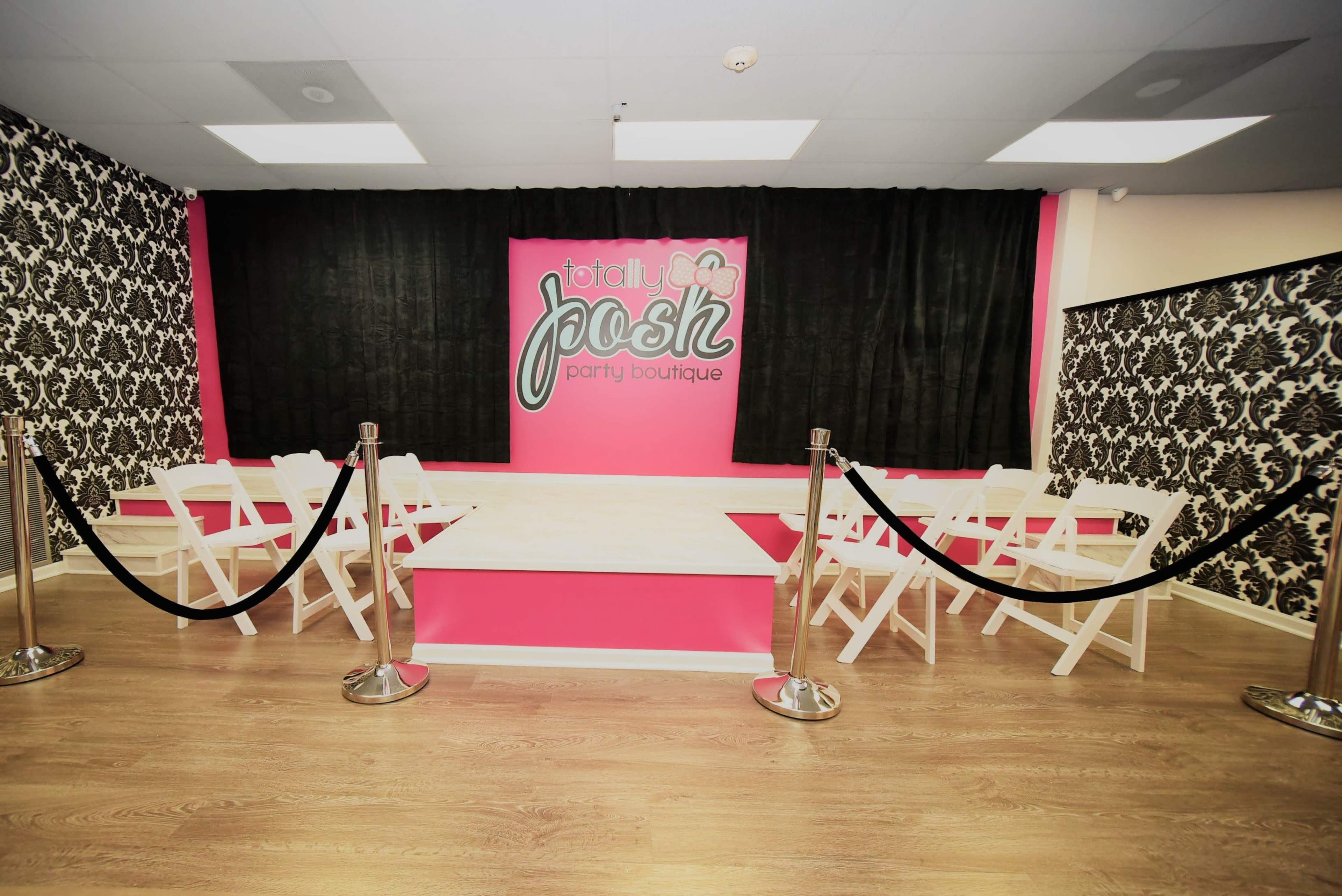 The image shows an interior space designed for parties, featuring a pink and black color scheme, with a stage area and white folding chairs arranged around it.
