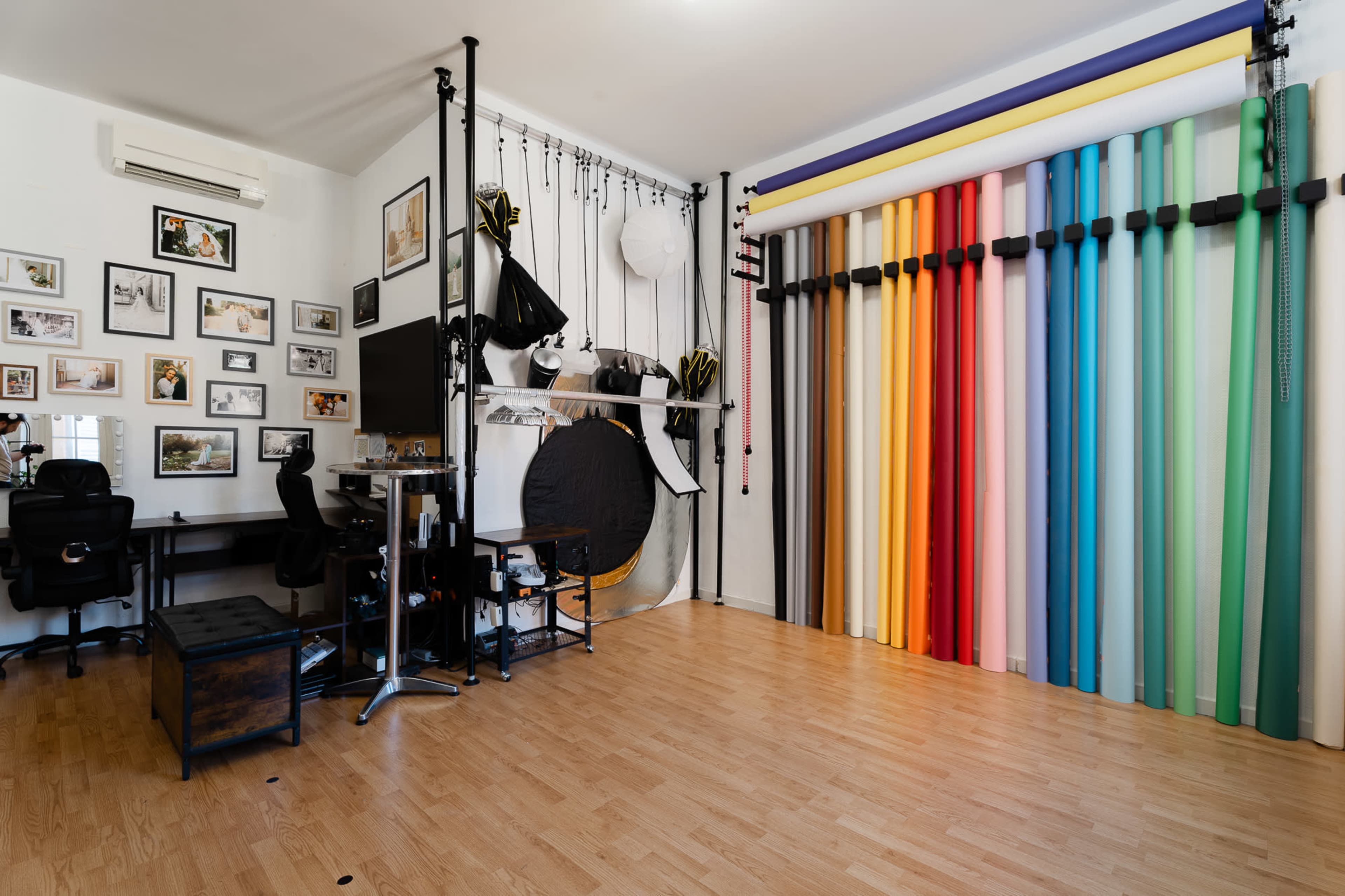The image depicts a photography studio featuring colorful backdrops, a desk with chairs, and framed photographs on the walls.