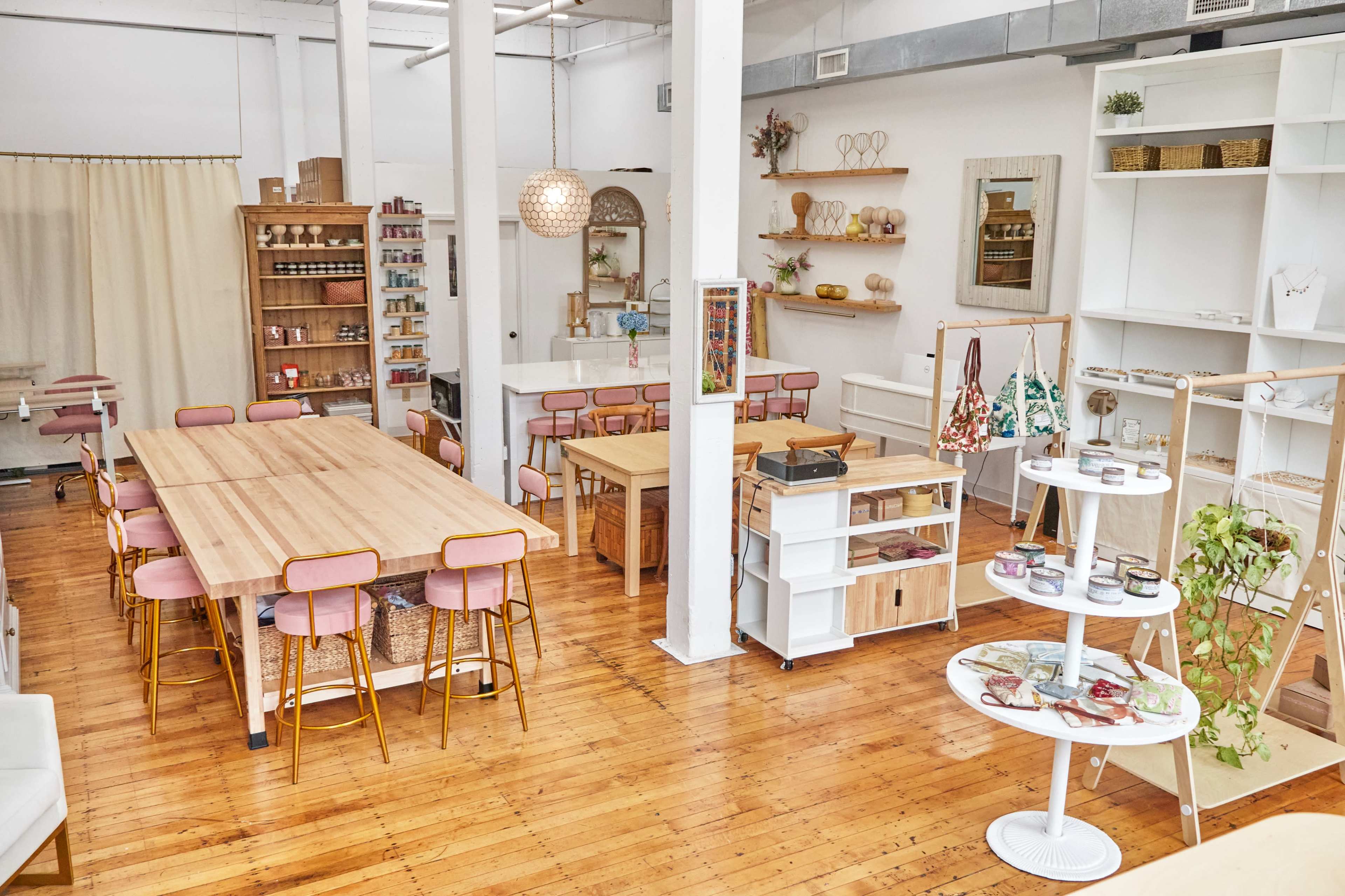 A bright, airy interior space with wooden floors, featuring a large communal table, various shelves displaying products, and seating areas.