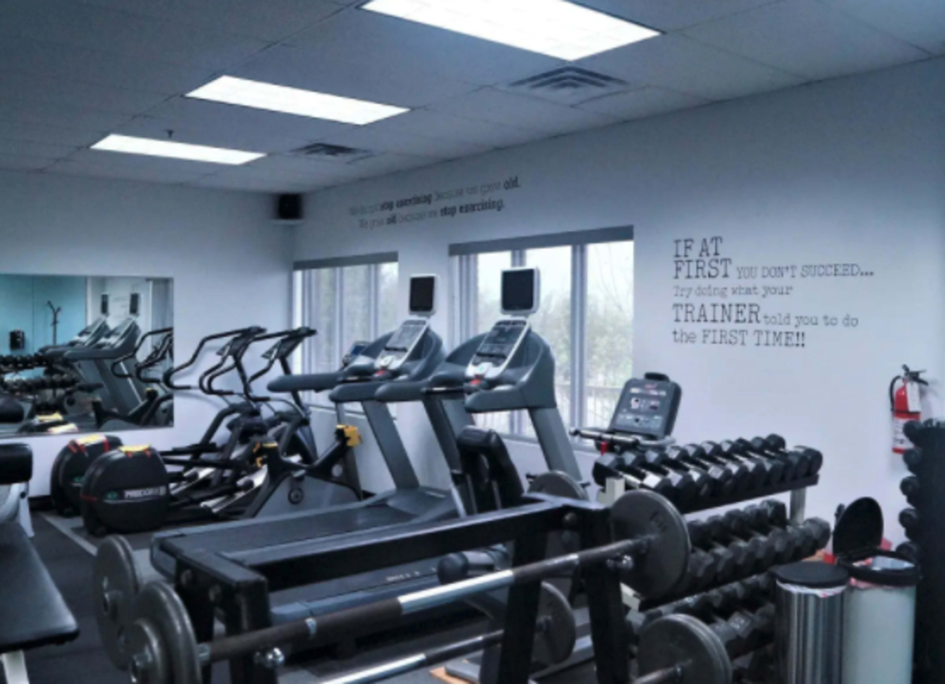 A gym interior with exercise equipment, including treadmills and free weights, along with a motivational quote on the wall.