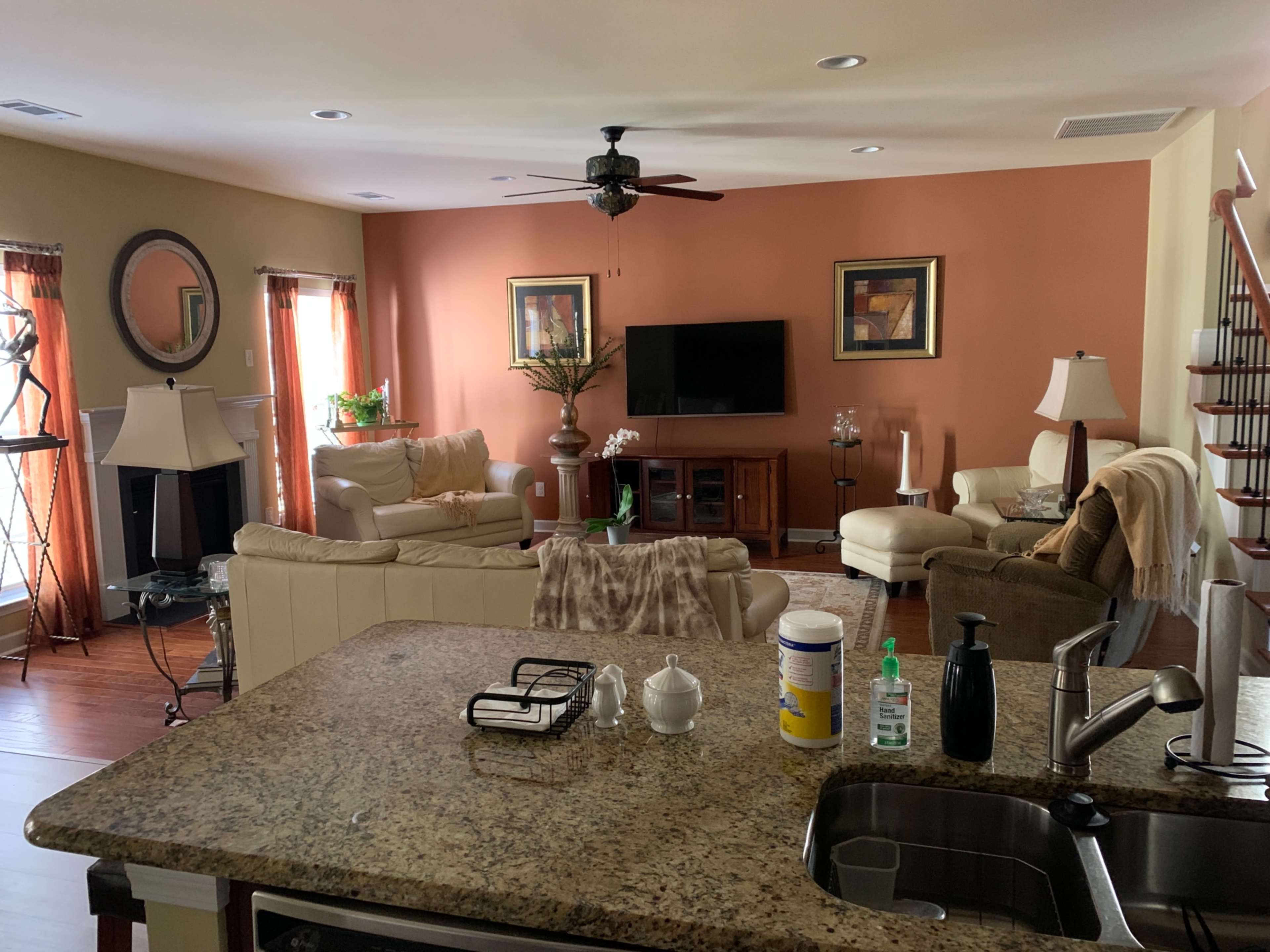 A living room with beige furniture, two lamps, a television on a wooden cabinet, and a staircase in the background.