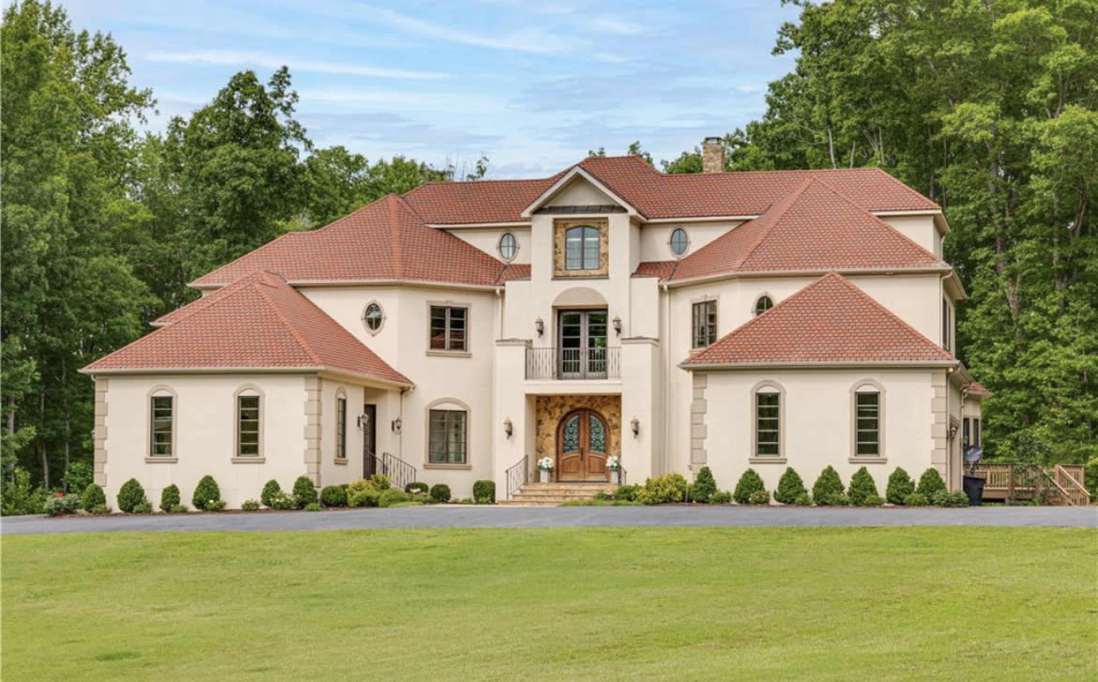 A large, two-story house with a red-tiled roof and a well-manicured lawn, surrounded by trees.