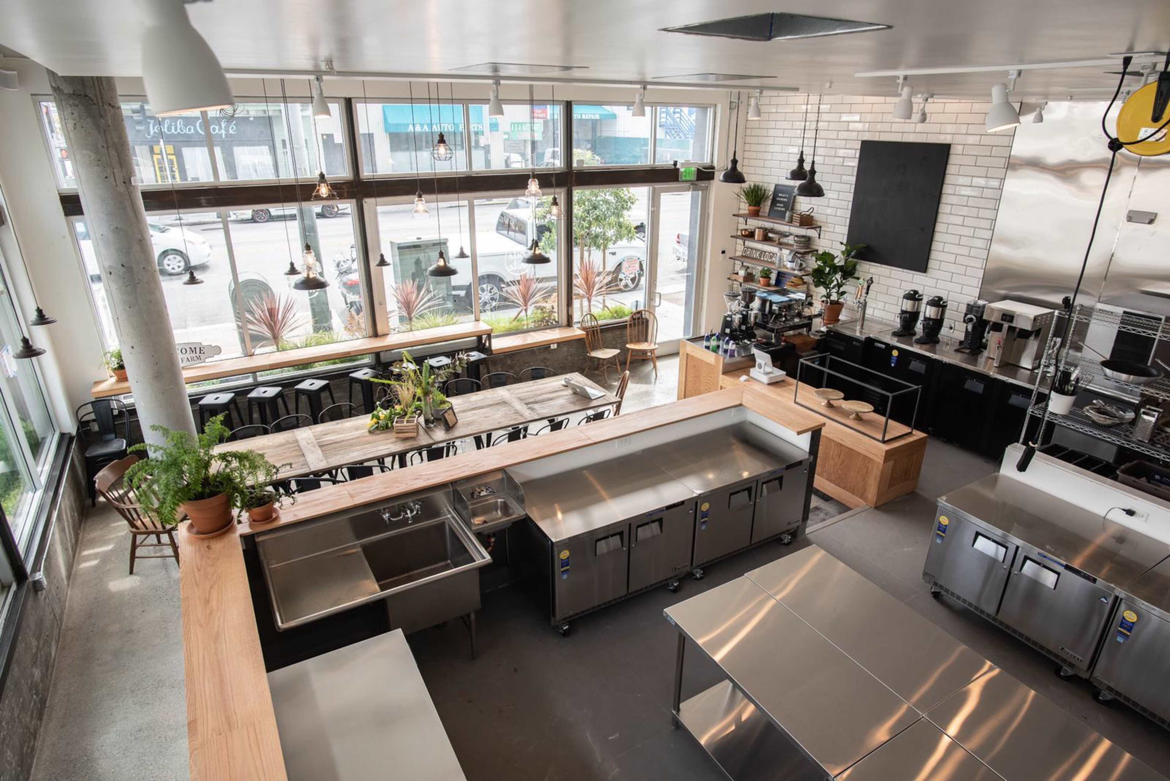 A modern café interior with large windows, wooden tables, and a stainless steel kitchen area.
