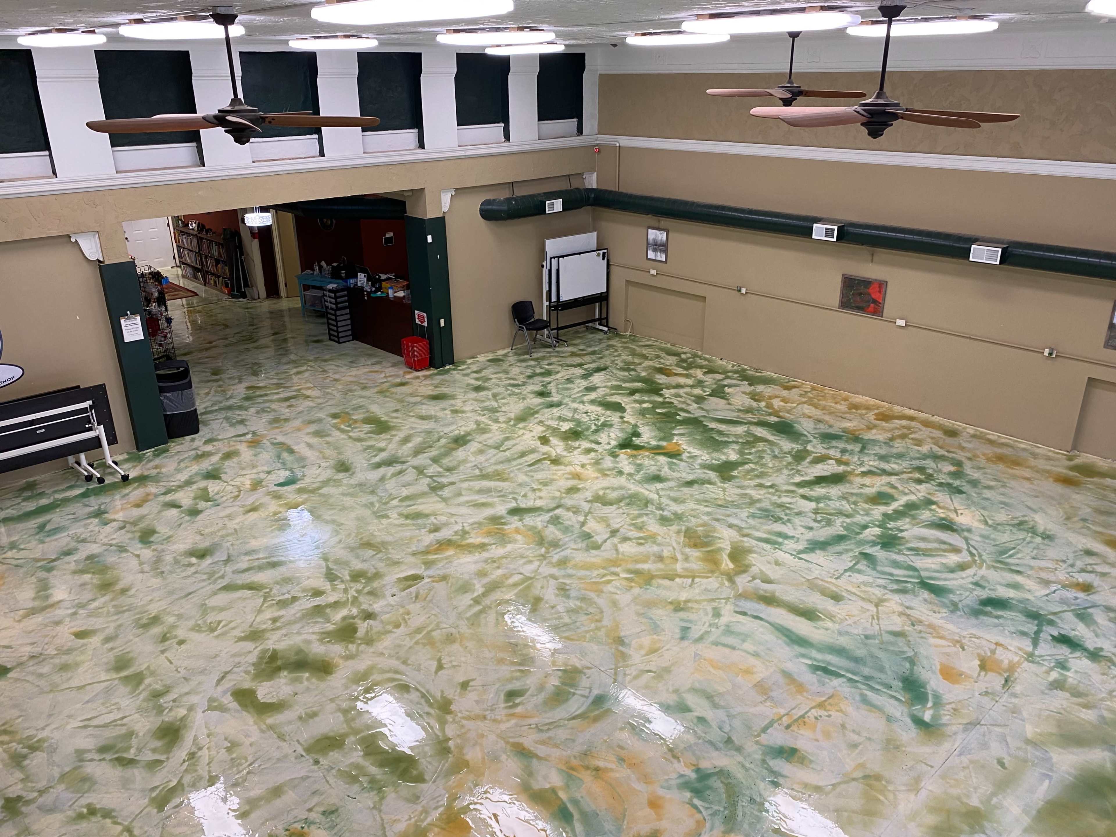 A large interior space with a floor featuring a marbled design in green and yellow tones, and two ceiling fans above.