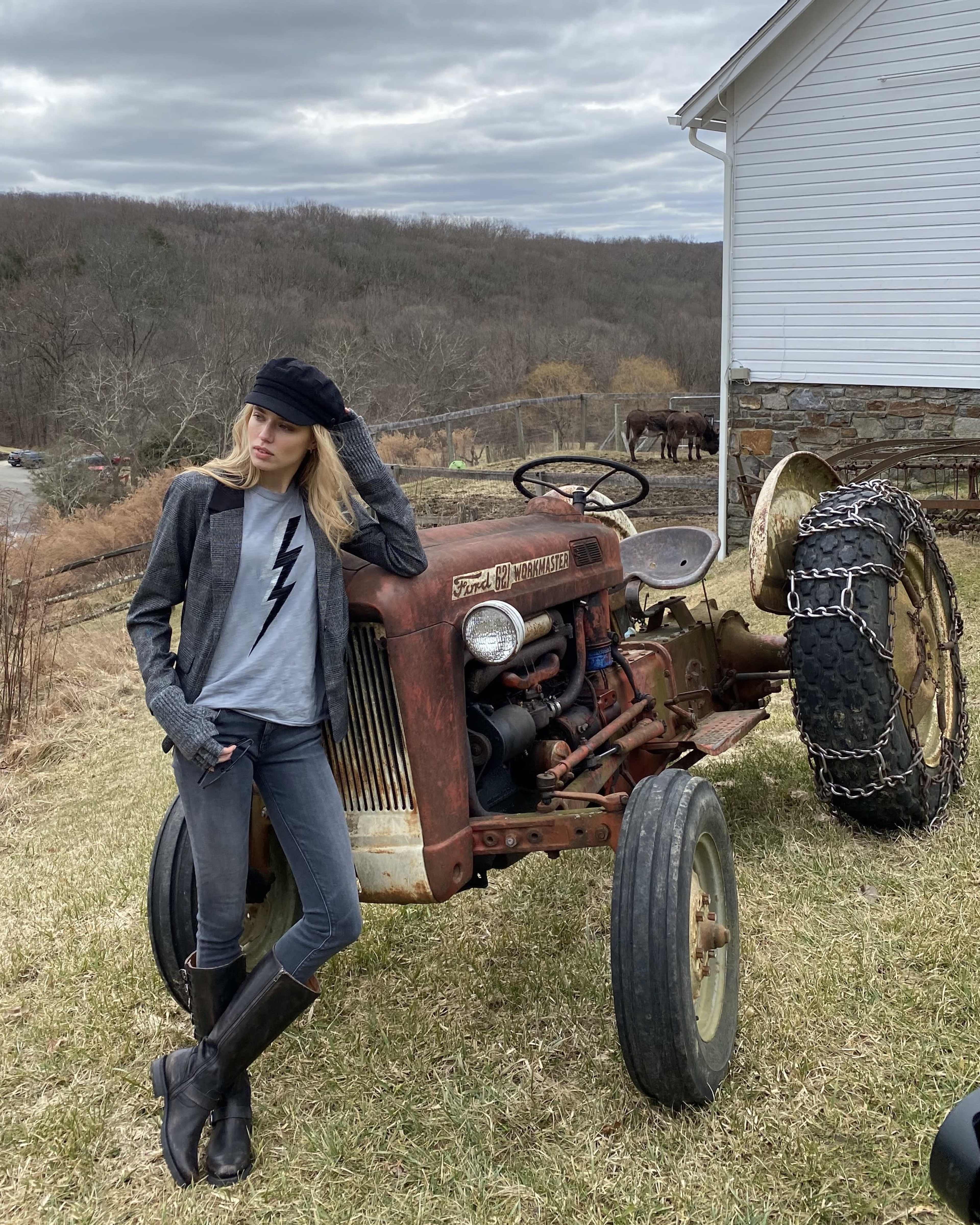 A person stands beside a vintage tractor on a grassy area with a gray sky in the background.