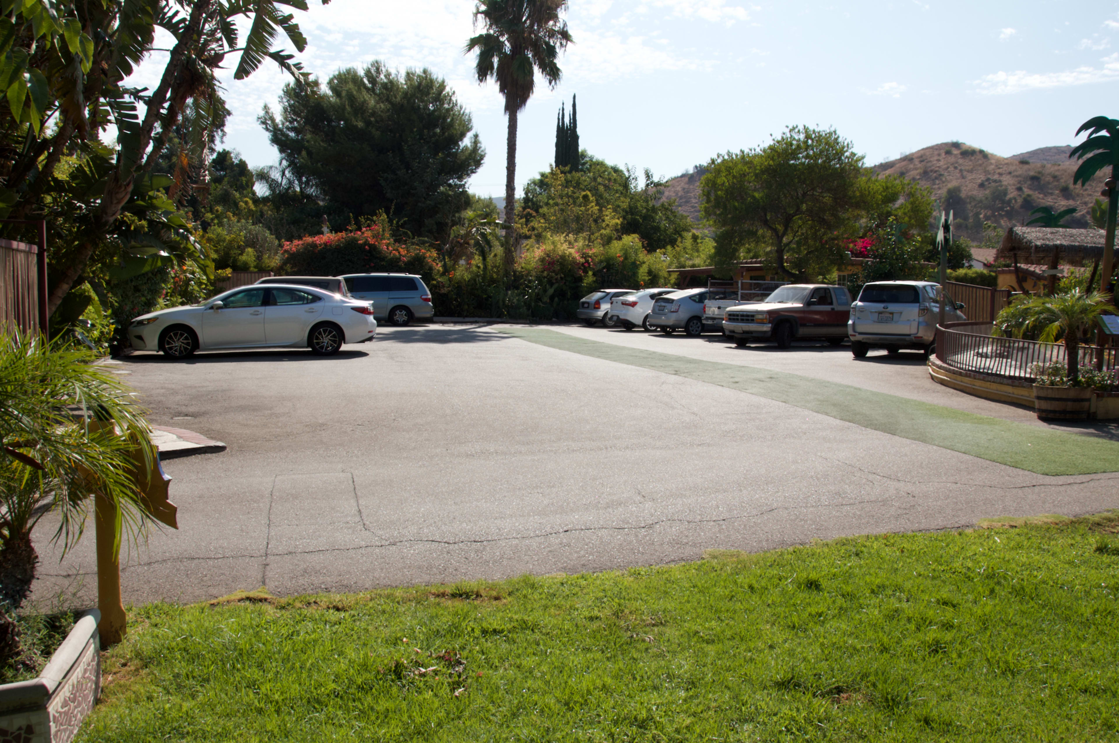 The image shows a parking lot with several parked cars surrounded by trees and hills in the background.