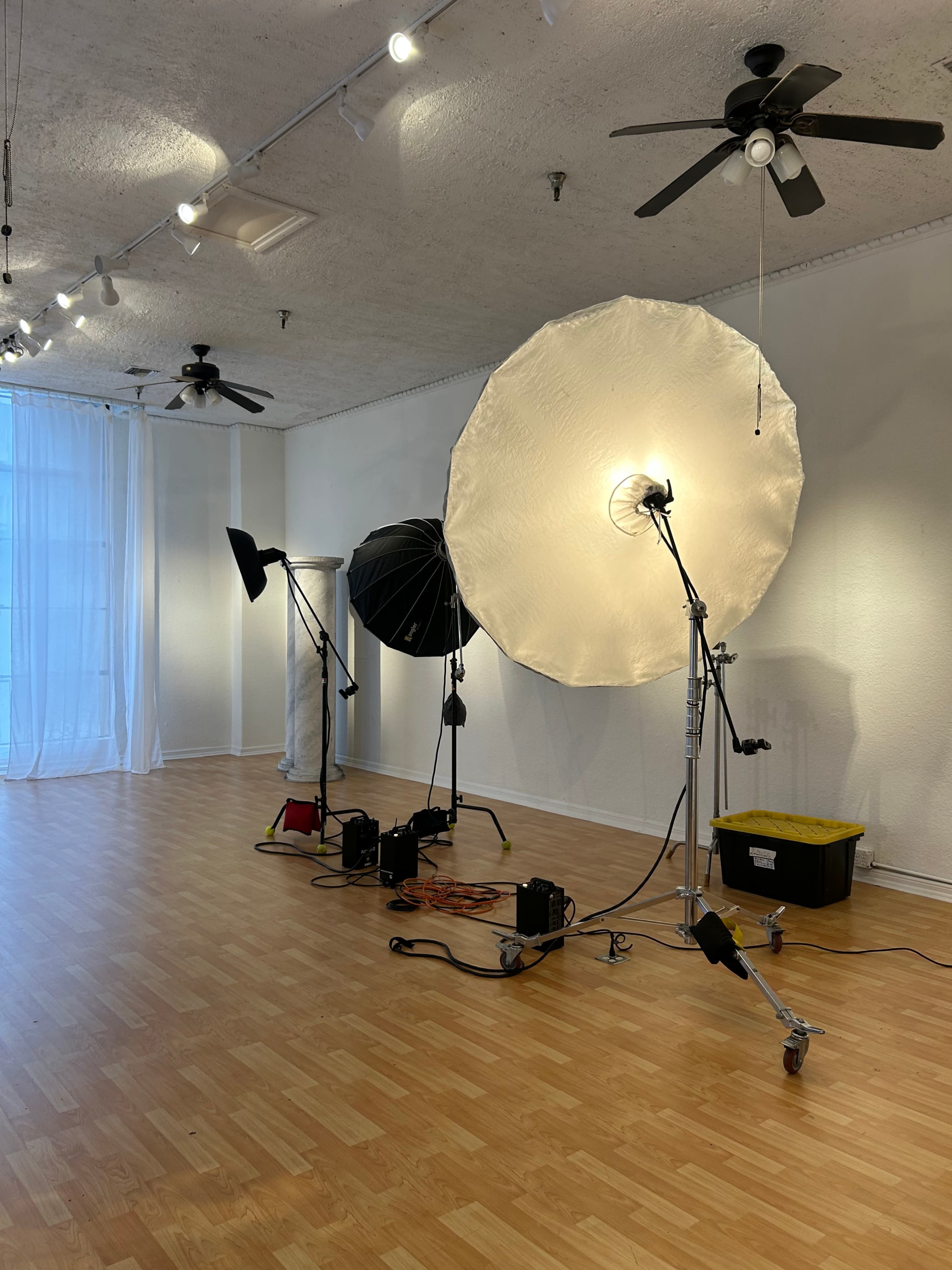 The image shows a photography studio with large softbox lights, a backdrop, and wooden flooring.