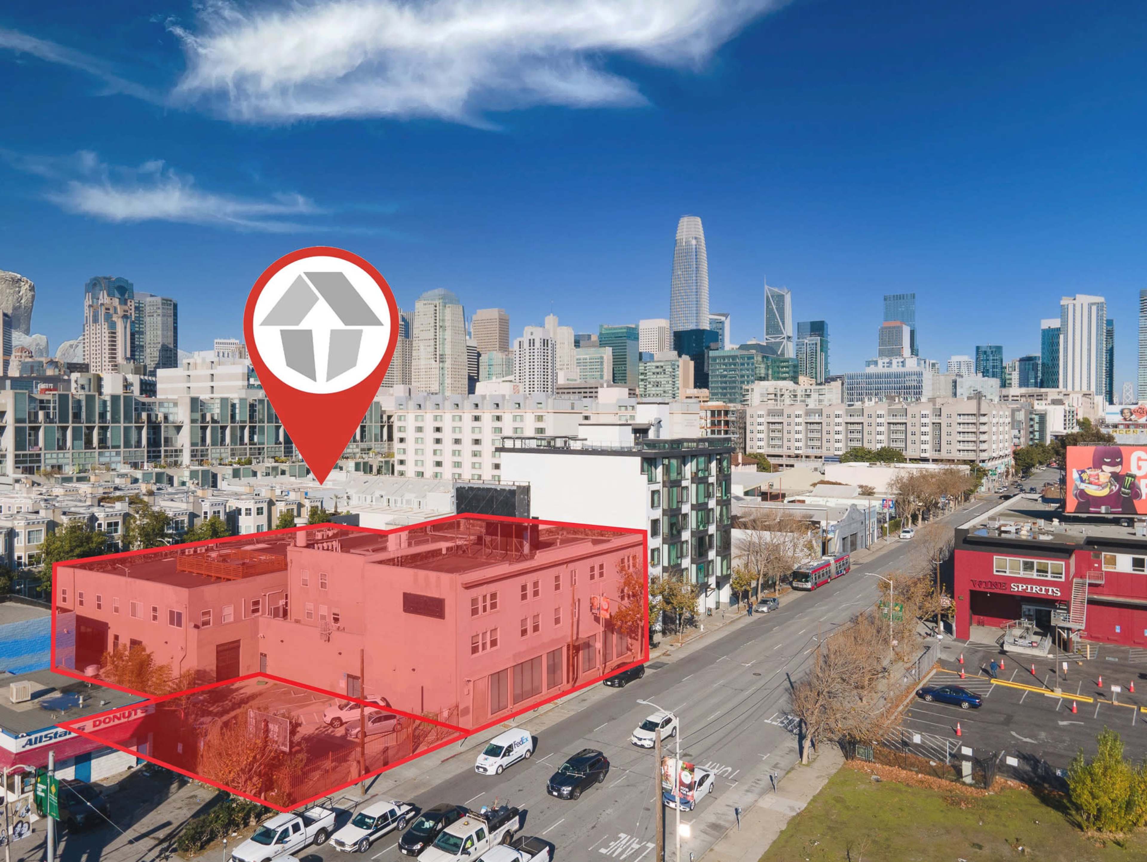 The image shows a cityscape featuring a building outlined in red, with a pin icon indicating its location, against a backdrop of tall skyscrapers in a blue sky.