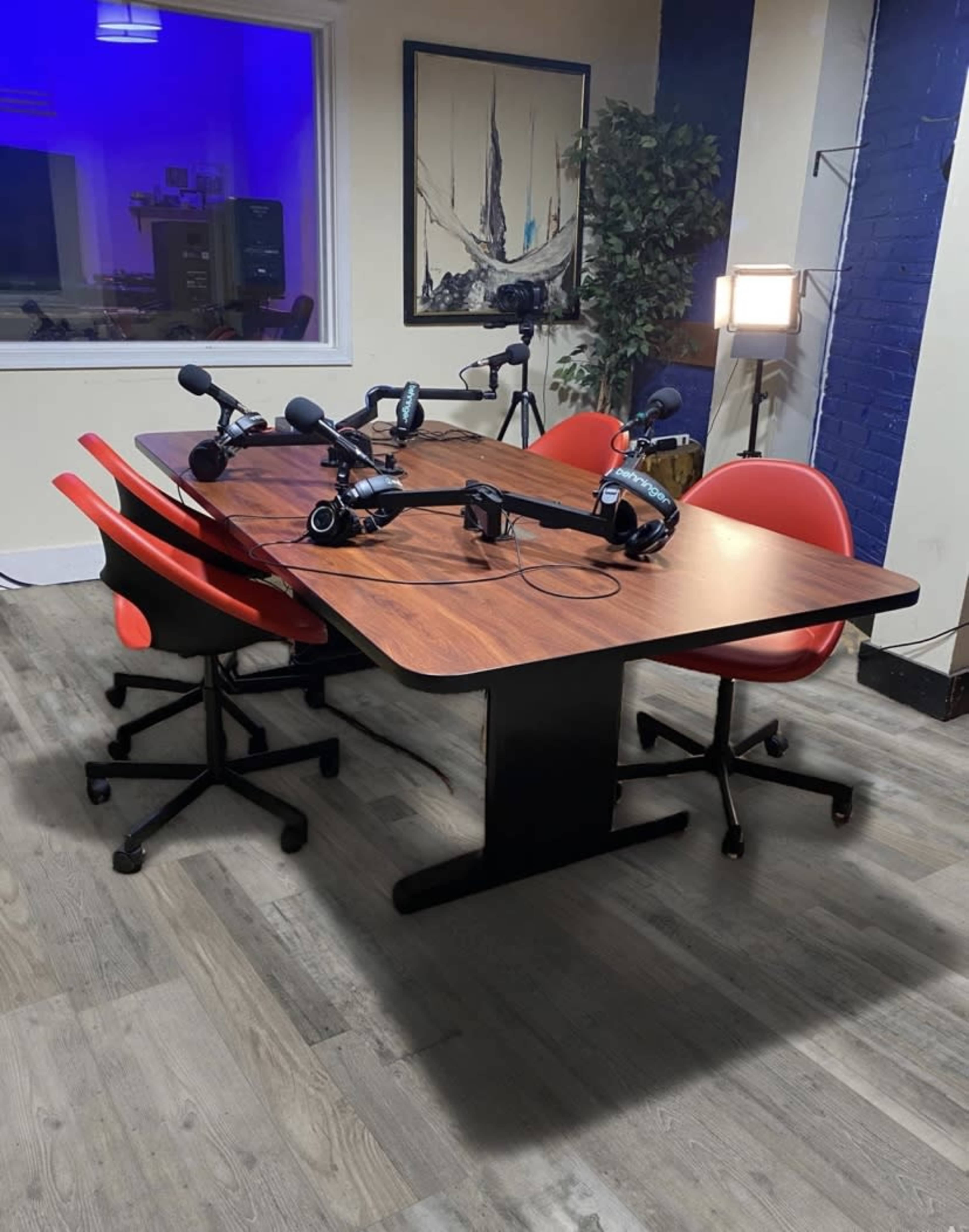 A round table with four chairs and microphones set up for a podcast recording in a brightly lit room.