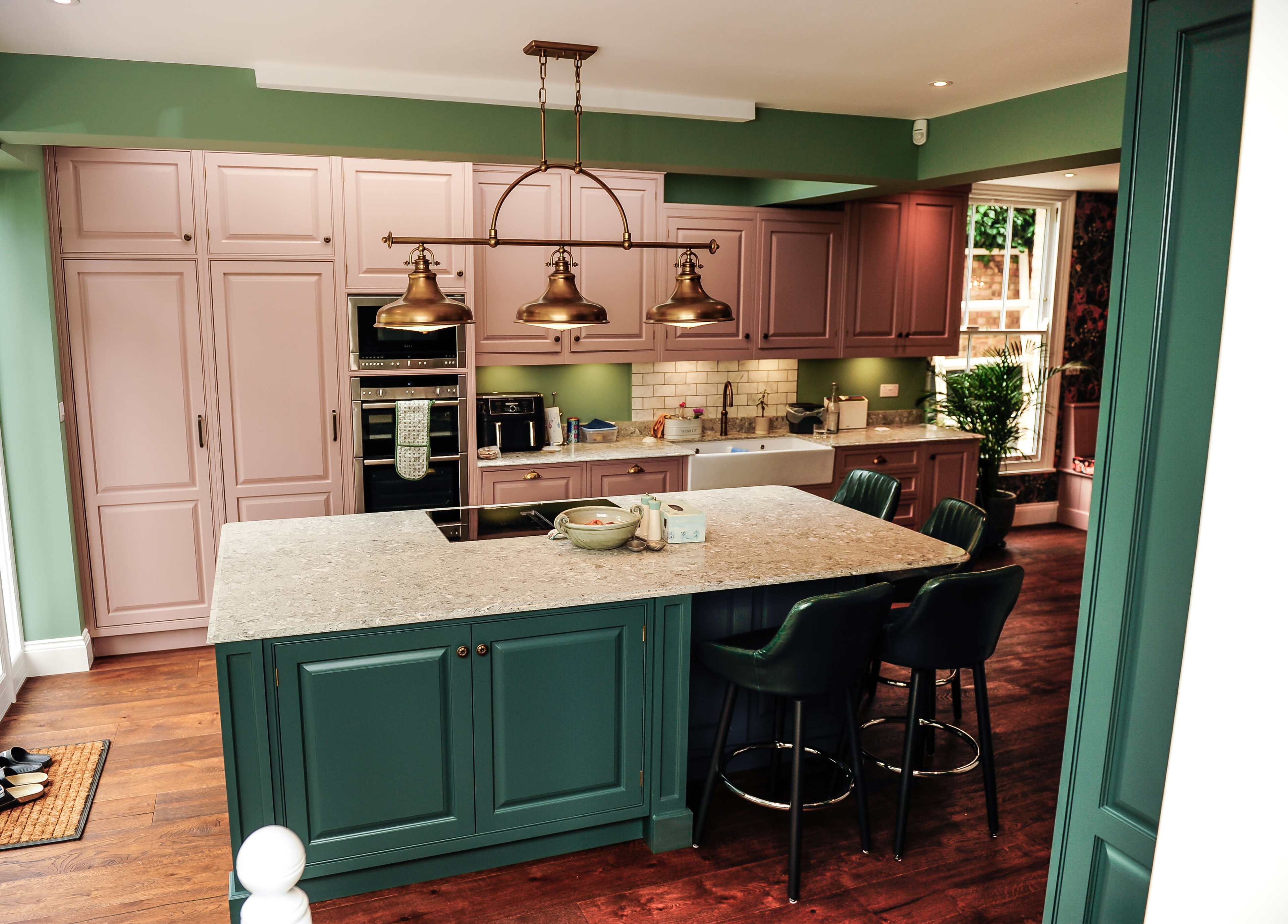 A modern kitchen featuring a large island with a stone countertop, green cabinetry, and pendant lighting above.