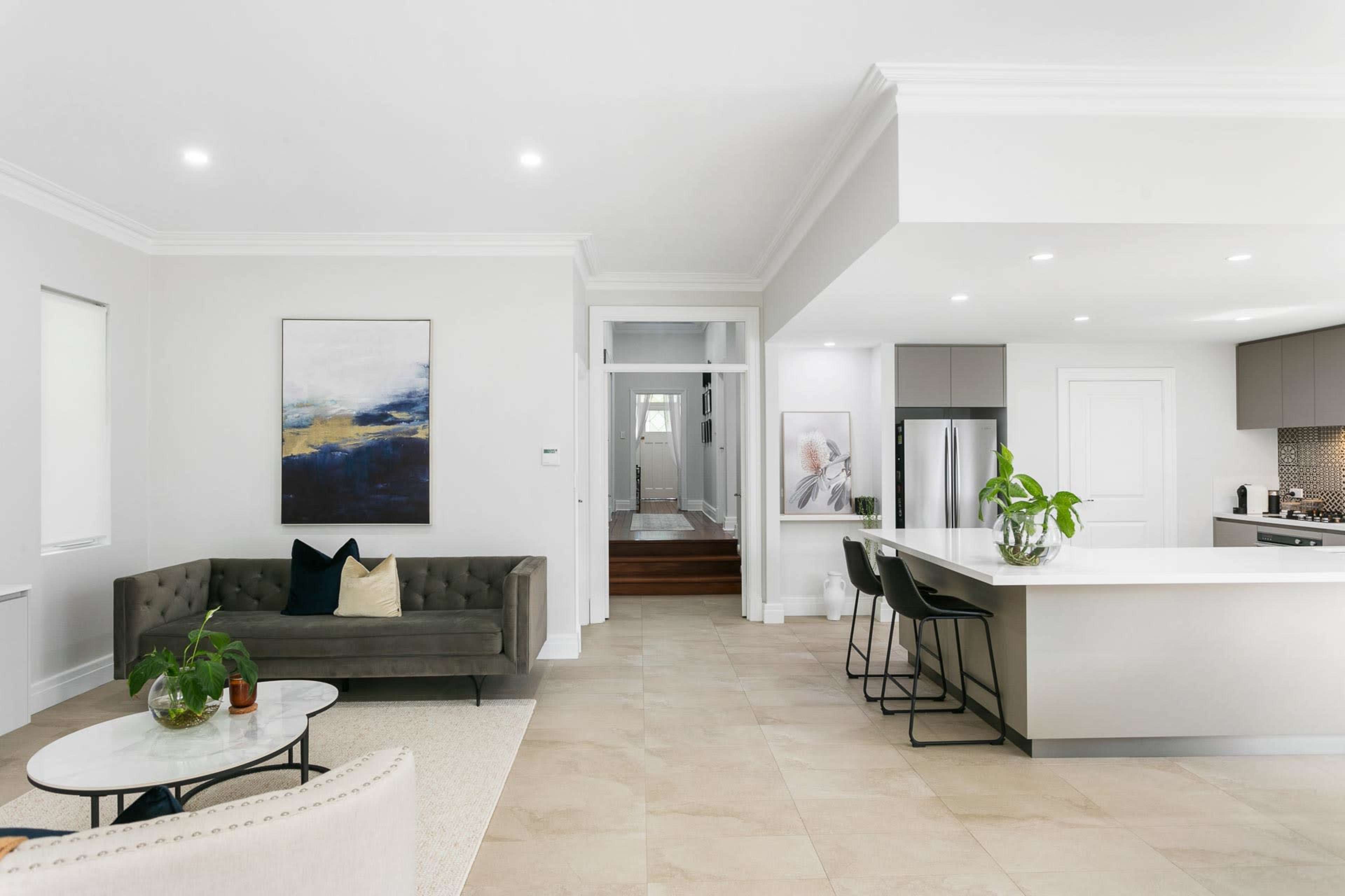 A modern living room with a gray sofa, a coffee table, and an open kitchen featuring a counter with bar stools and stainless steel appliances.