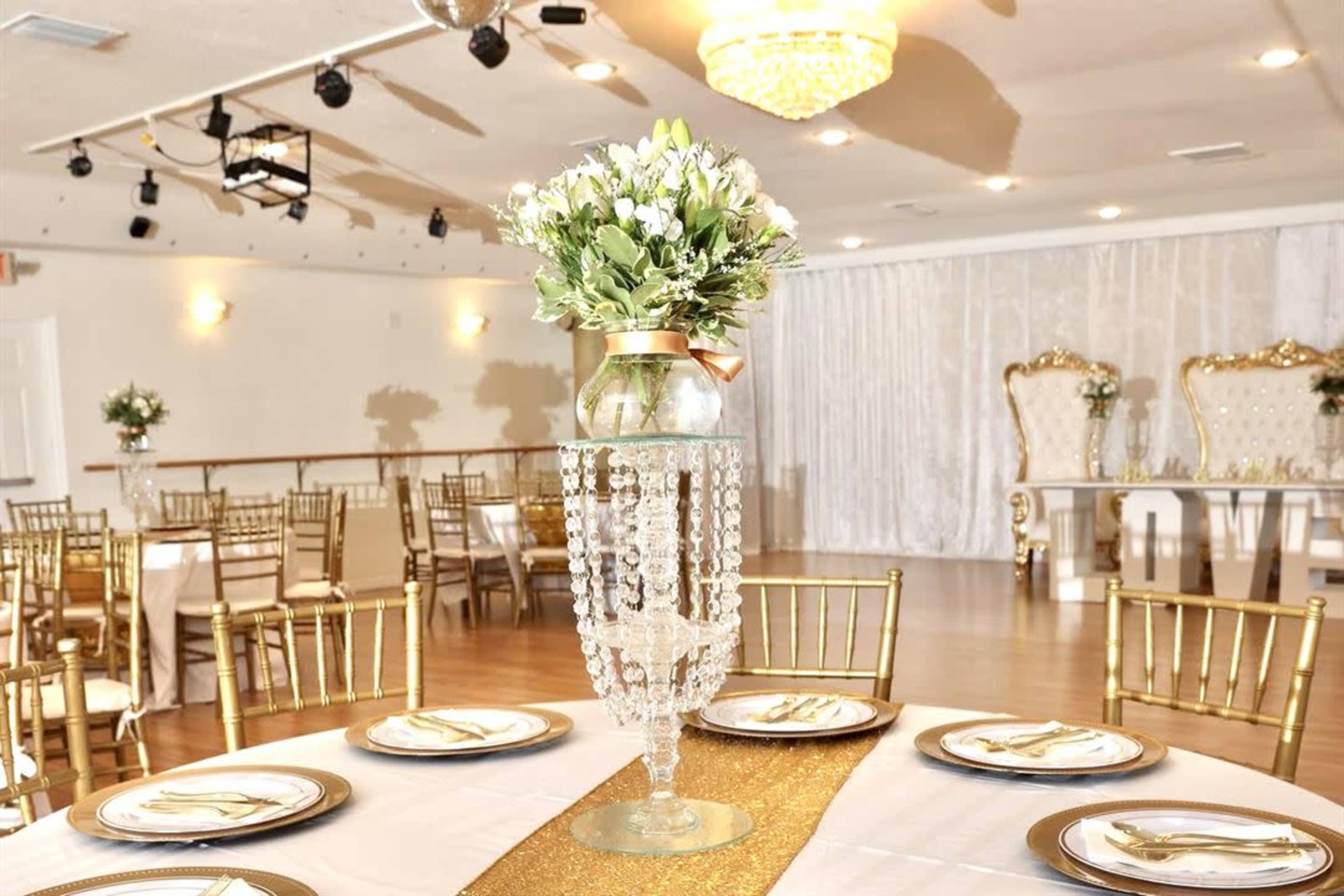 A banquet hall is set up for an event with round tables adorned with elegant centerpieces and golden chairs.
