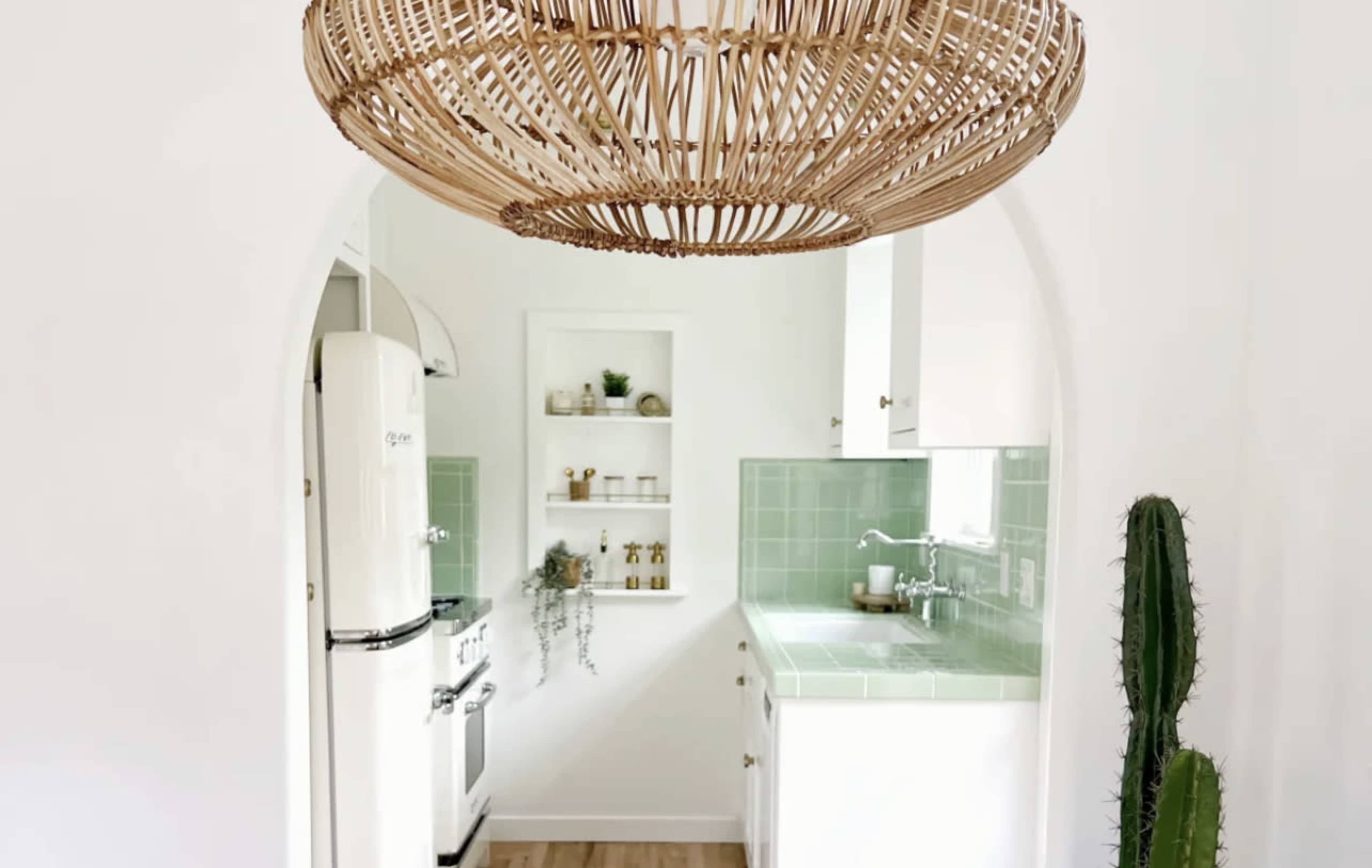 A kitchen is visible through an archway, featuring a retro fridge, green tiled backsplash, and a large woven light fixture overhead.