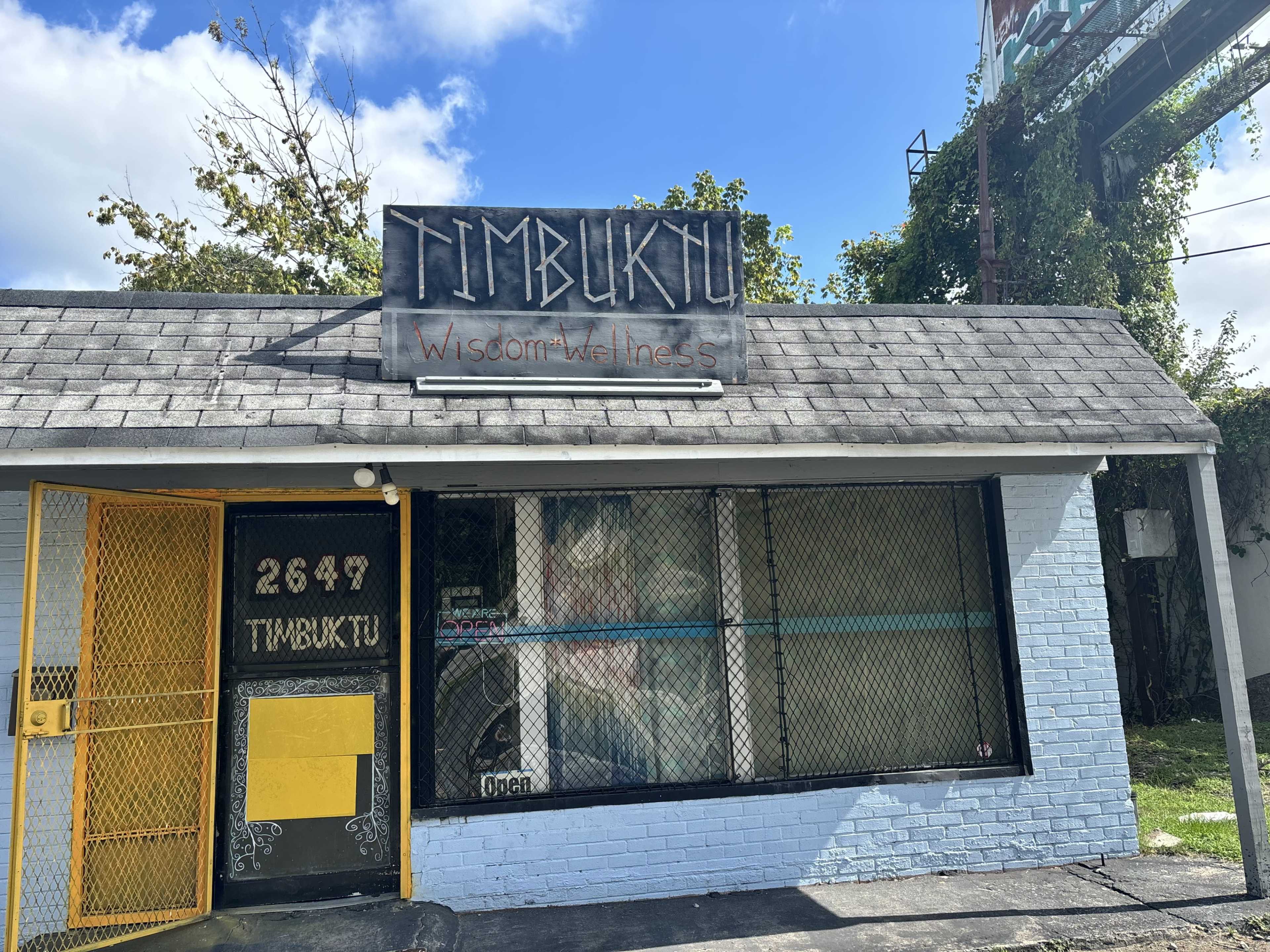 The image shows a storefront named "Timbuktu," featuring a yellow door and a mural visible through the front window.
