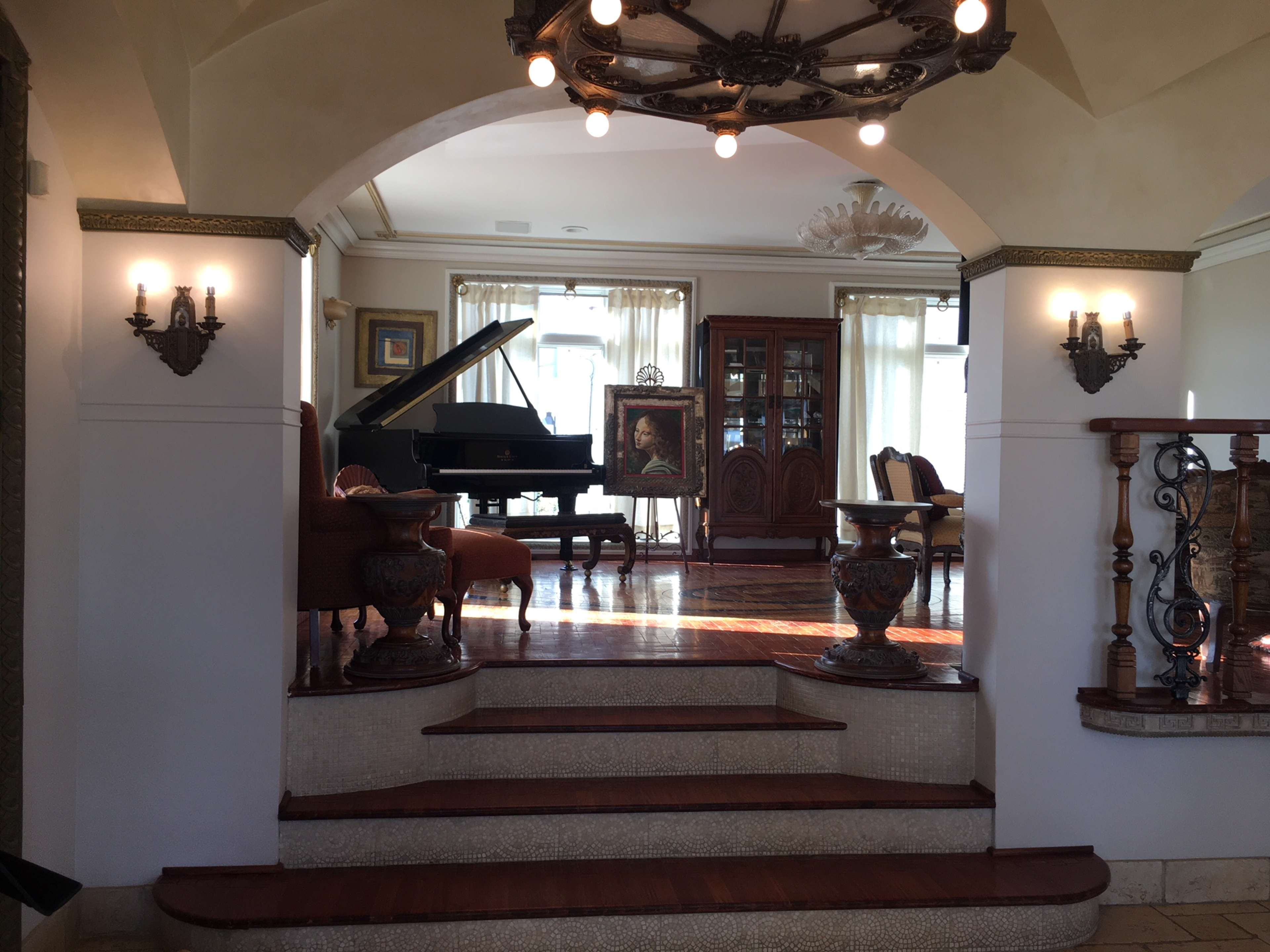 A spacious living room with a grand piano, elegant furniture, and large windows allowing natural light.