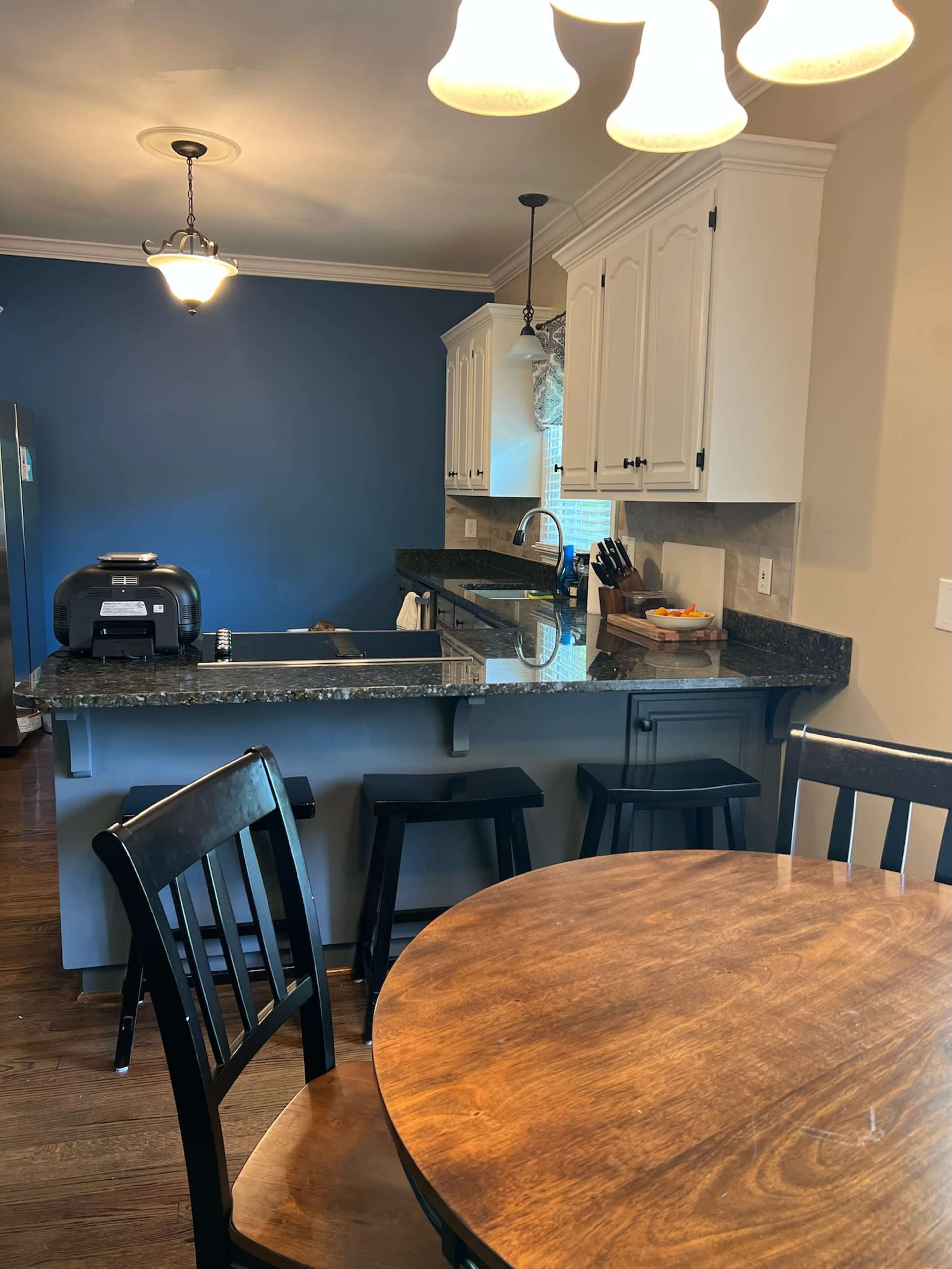 A kitchen with white cabinets, a dark countertop, and a dining table surrounded by chairs.