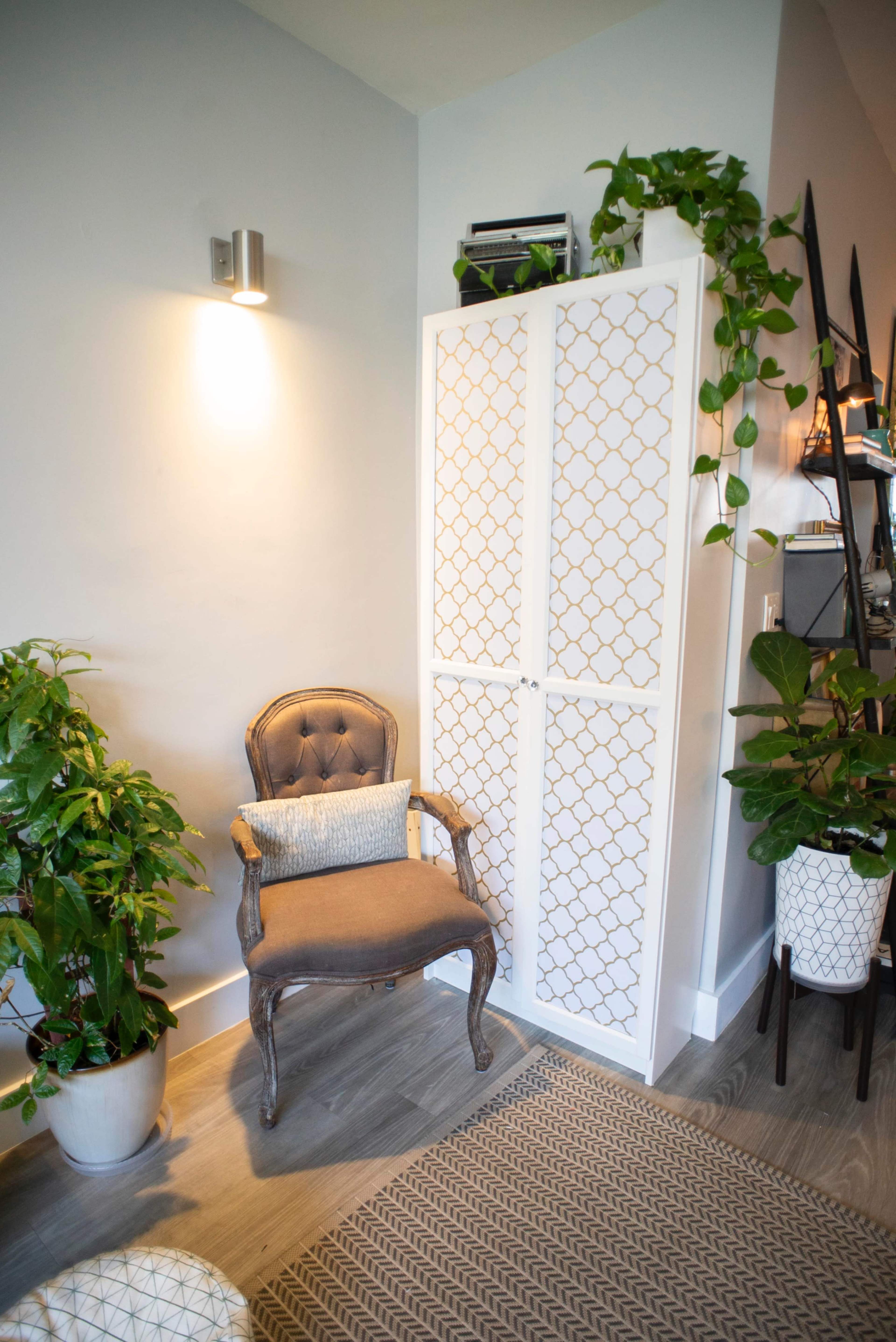 A cozy corner features a decorative cabinet, a vintage armchair, and lush greenery in pots.