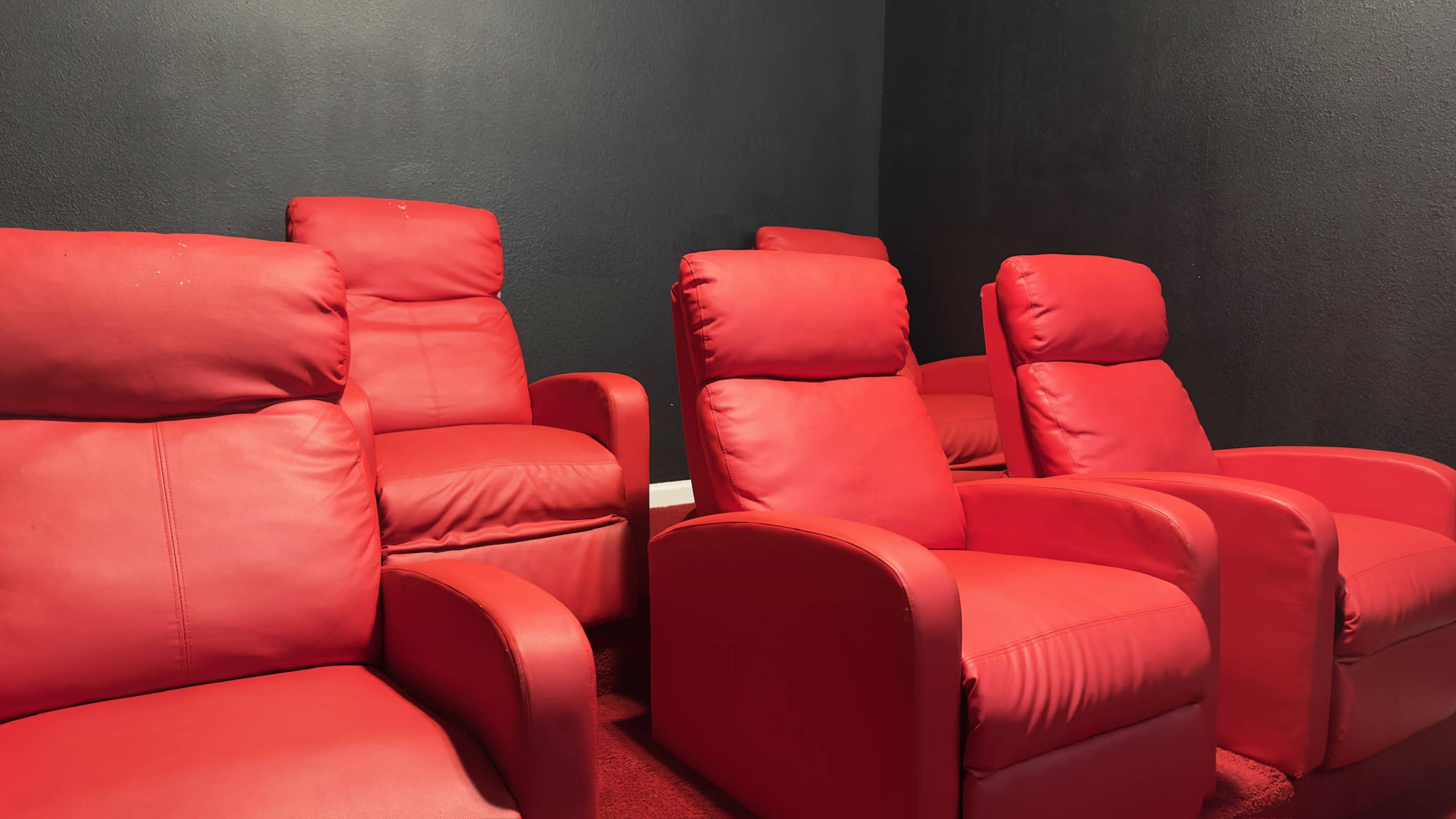 A row of red leather recliner chairs against a dark wall in a resting area.