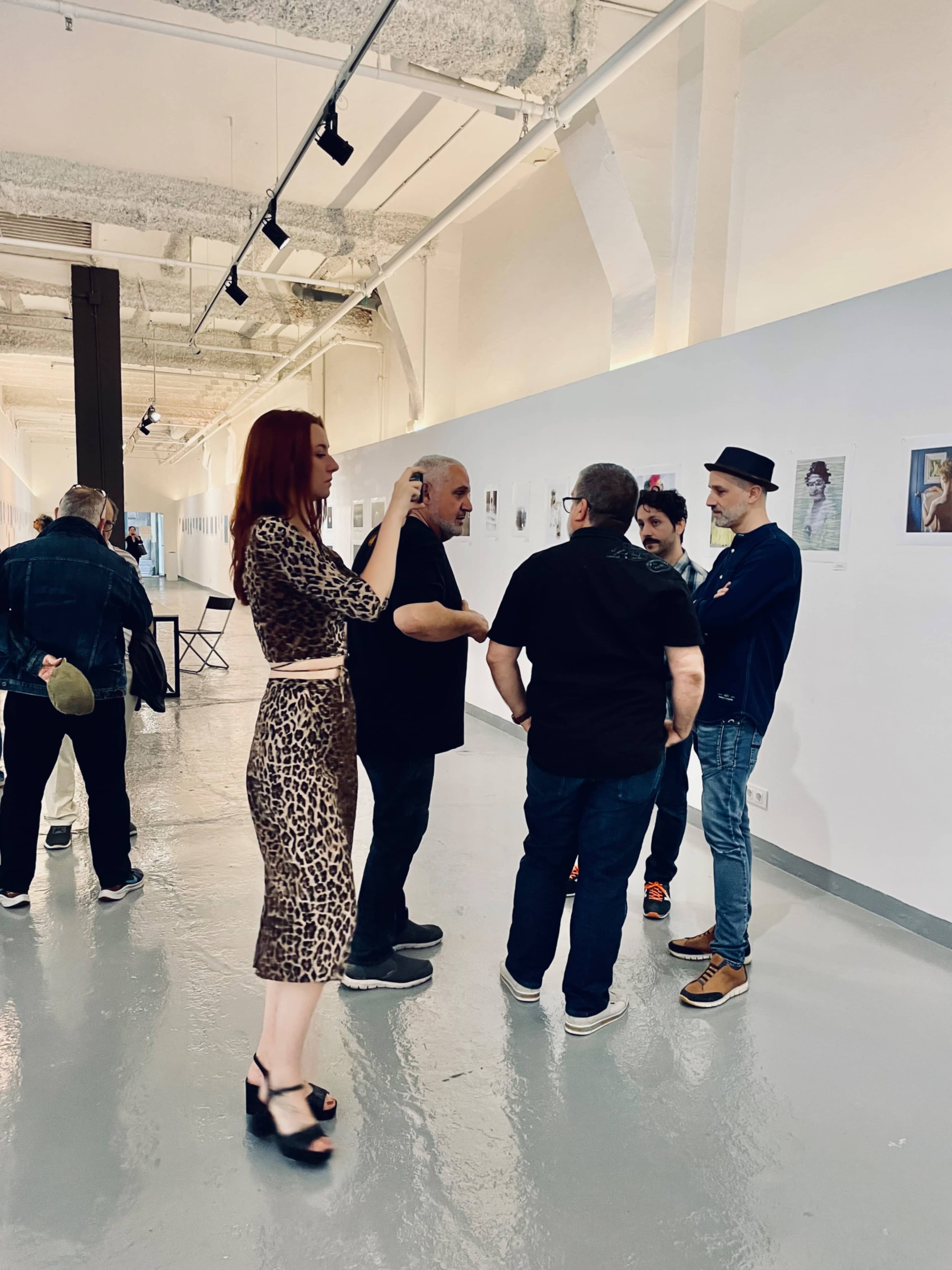 A group of five people converse in an art gallery with photography displayed on the walls.
